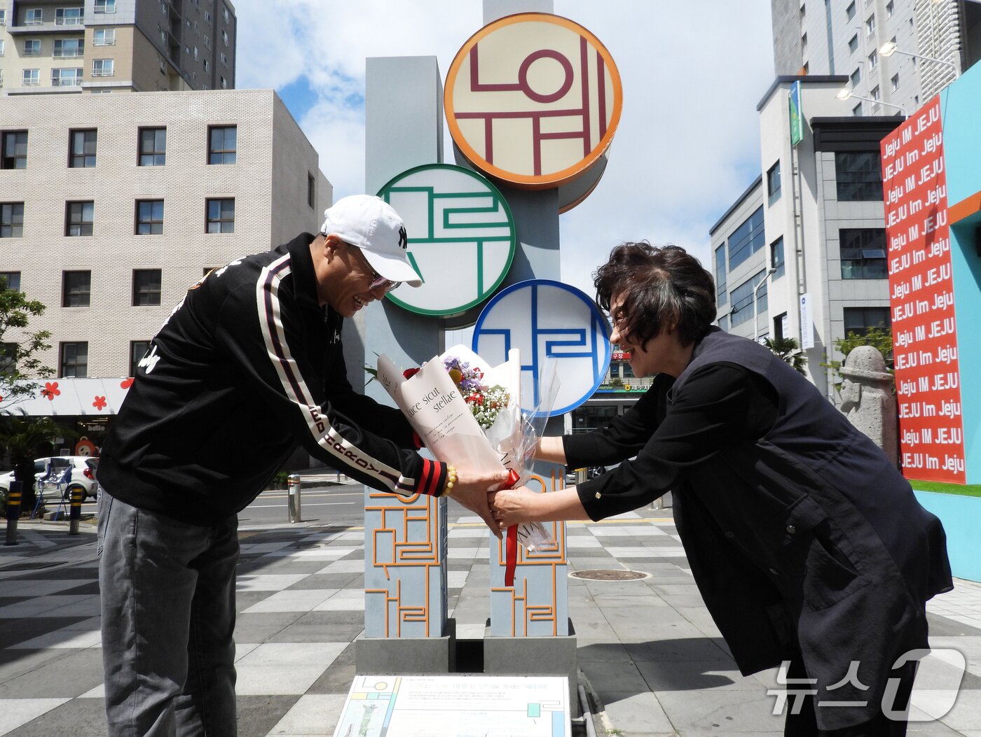 본문 이미지 - 28일 오후 제주시 연동 누웨마루 거리에서 열린 '제주드림타워-누웨마루거리 상생버스' 운행 기념식에서 신애복 누웨마루거리 상점가 상인회장이 한 외국인 탑승객에게 꽃다발을 전달하고 있다.