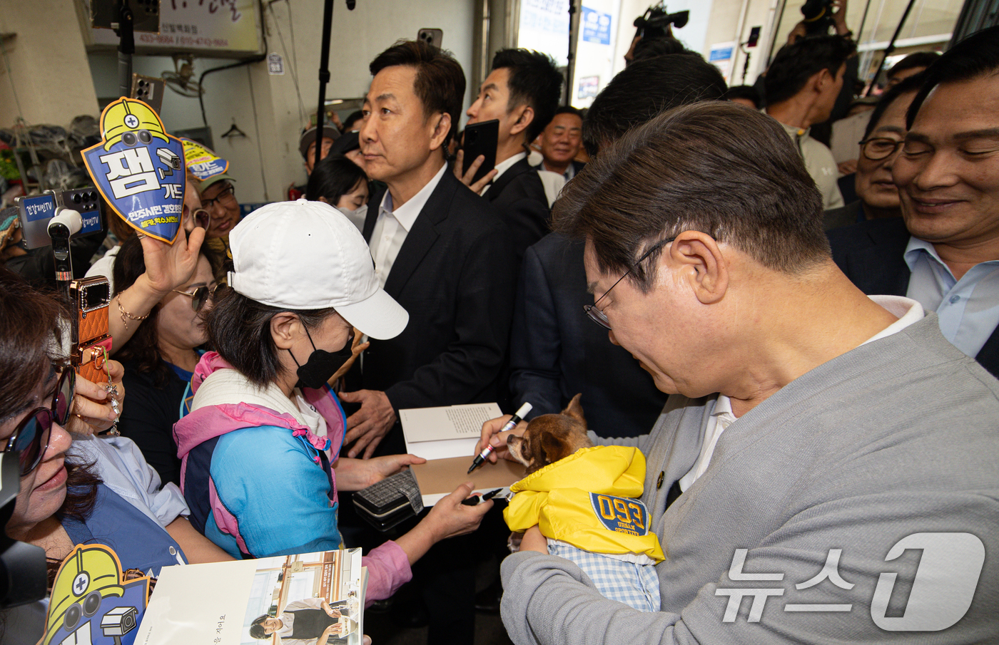 (강진=뉴스1) 이재명 기자 = 경청투어에 나선 이재명 더불어민주당 대통령 후보가 11일 오전 전남 강진군 강진시장에서 반려견을 품에 안고 시민 요청에 사인하고 있다. 2025.5 …