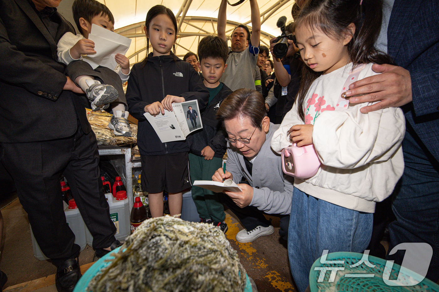 (강진=뉴스1) 이재명 기자 = 경청투어에 나선 이재명 더불어민주당 대통령 후보가 11일 오전 전남 강진군 강진시장에서 어린이의 요청으로 책에 사인하고 있다. 2025.5.11/뉴 …