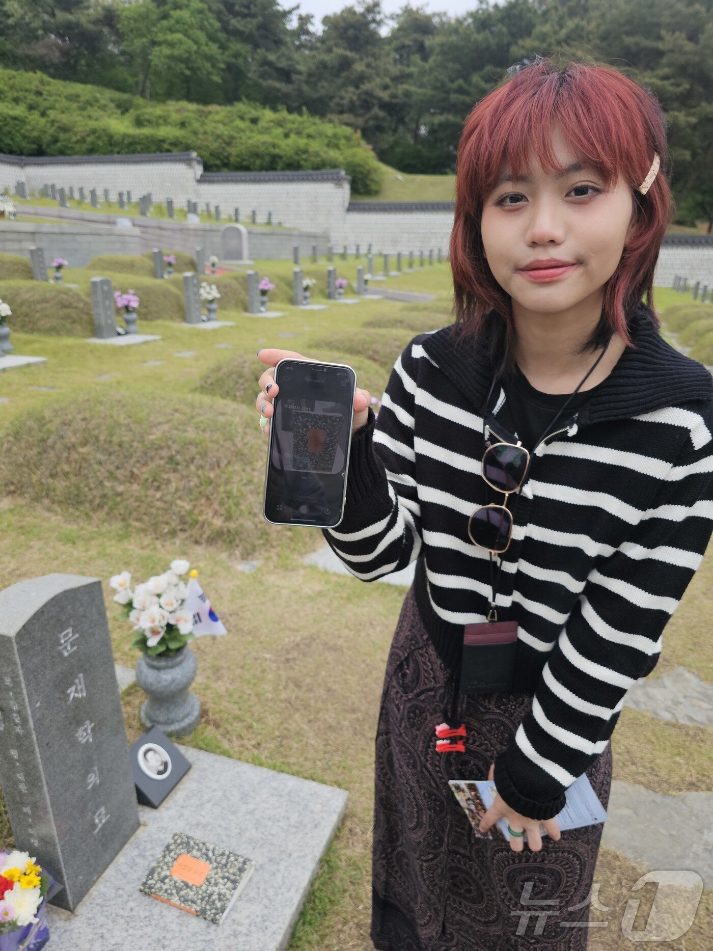 본문 이미지 - 11일 광주 북구 운정동 5·18민주묘역에서 태국 대학생 나띠씨가 소설 ‘소년이 온다’의 실제 모델인 문재학 군의 묘소에서 자신의 휴대폰 속 ‘소년이 온다’사진을 들어보이고 있다. 나띠씨는 한국 드라마 ‘오월의 청춘’을 시작으로 영화 ‘택시운전사’를 보고 5·18을 알게 됐다. 2025.5.11/뉴스1 ⓒ News1 서충섭 기자