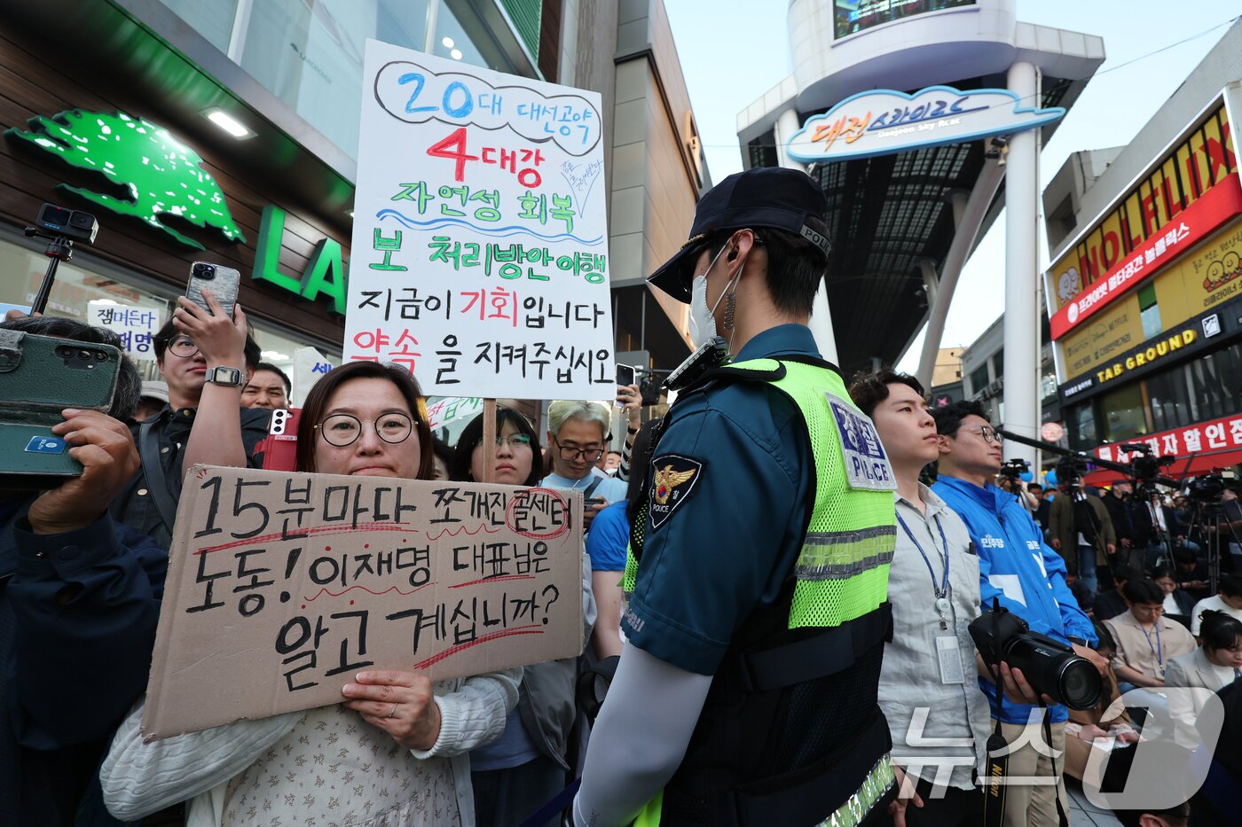 본문 이미지 - 이재명 더불어민주당 대통령 후보가 제21대 대통령 선거 공식 선거운동 첫날인 12일 오후 대전 중구 으능정이거리 스카이로드에서 유세를 하는 가운데 일부 시민들이 4대강 회복 등을 요구하는 피켓을 들고 있다. 2025.5.12/뉴스1 ⓒ News1 안은나 기자
