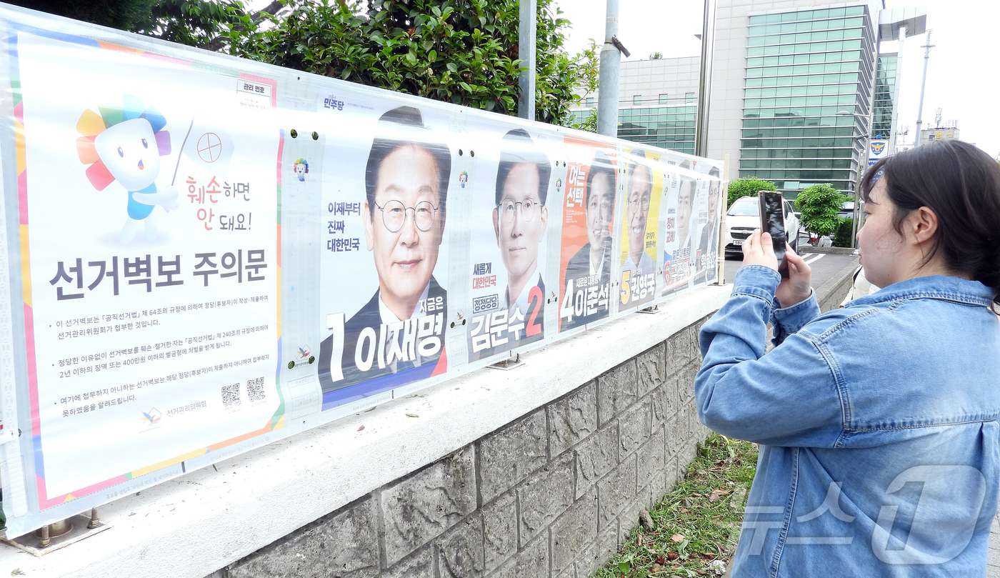 (제주=뉴스1) 오미란 기자 = 한 시민이 15일 오후 제주시 이도2동 통계교육원 제주수련원 정문 울타리에 부착된 제21대 대통령 선거 후보자 선거벽보를 살피고 있다. 2025.5 …