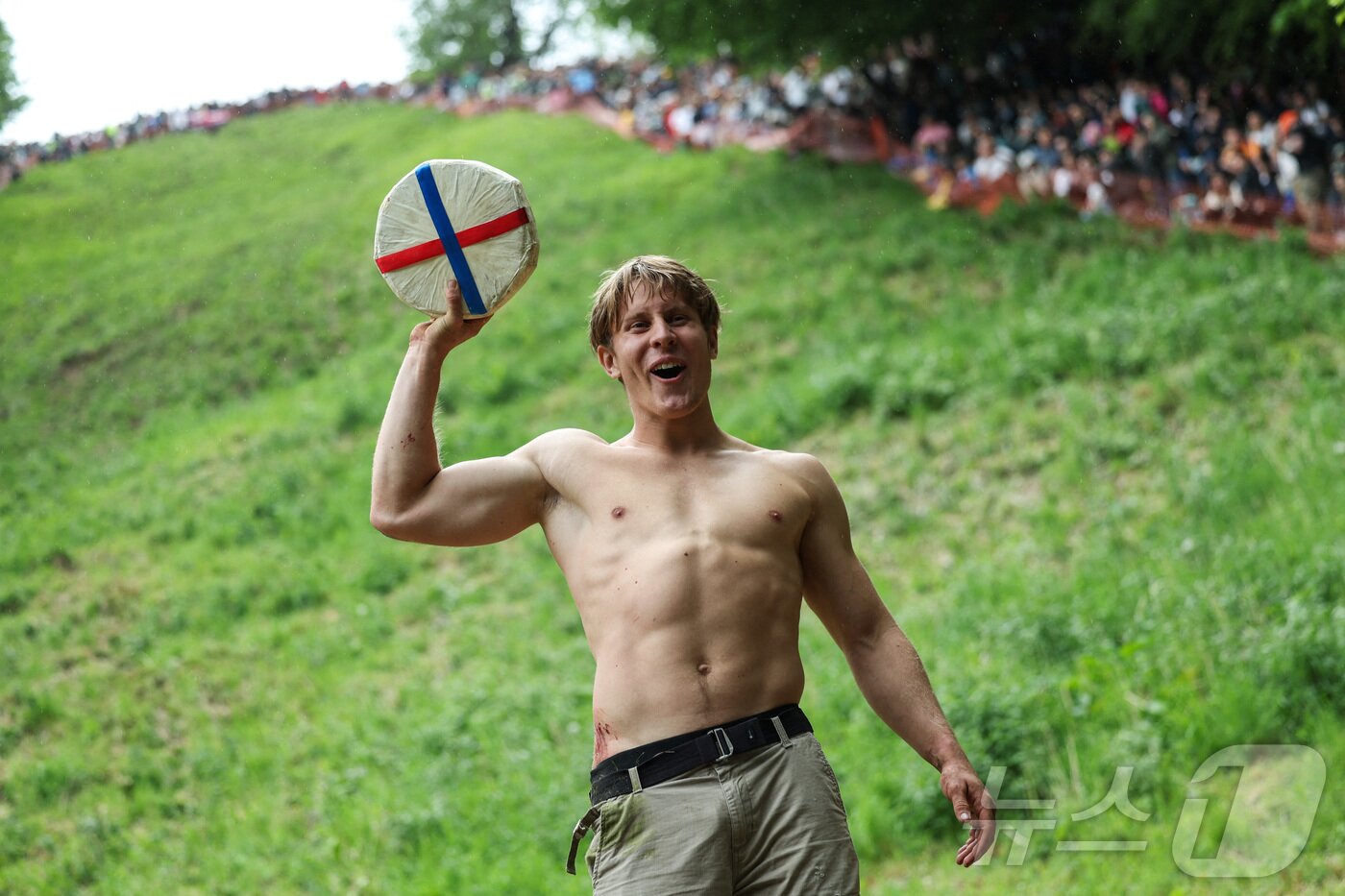 본문 이미지 - 26일(현지시간) 영국 브록웍스의 쿠퍼스 힐에서 열린 '구르는 치즈 잡기' 대회에서 우승한 톰 코프케가 치즈 바퀴를 들고 환호하고 있다.  ⓒ 로이터=뉴스1