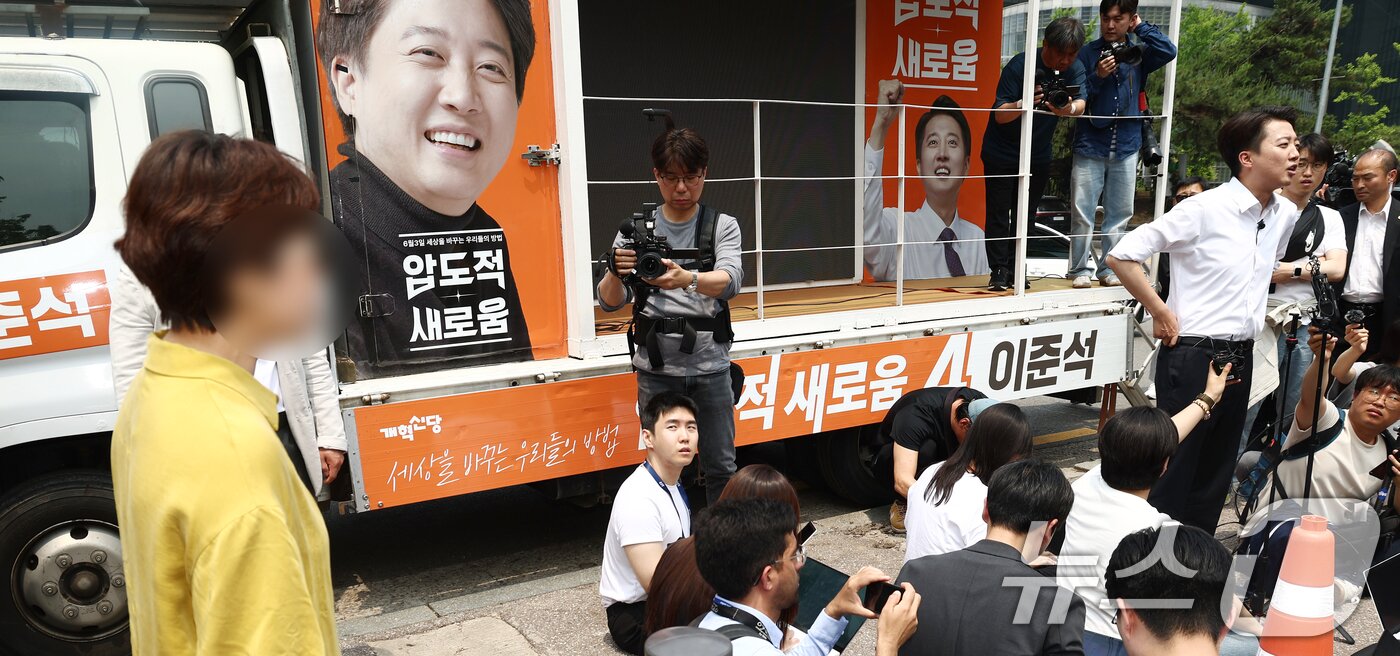 본문 이미지 - 이준석 개혁신당 대통령 후보가 28일 서울 영등포구 여의도공원에서 유세를 마치고 취재진 질의에 답변하고 있는 가운데 한 시민이 이 후보가 전날 토론회에서 여성 신체를 묘사 발언을 한 것에 대해 항의하고 있다. 2025.5.28/뉴스1 ⓒ News1 김민지 기자