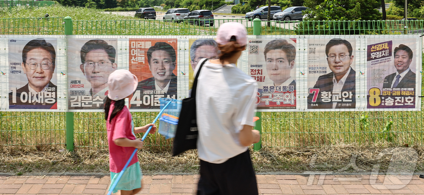 (화성=뉴스1) 김도우 기자 = 제21대 대통령선거를 이틀 앞둔 1일 경기 화성시 시내 한 거리에서 시민들이 후보자들의 선거 벽보 앞으로 지나고 있다. 2025.6.1/뉴스1