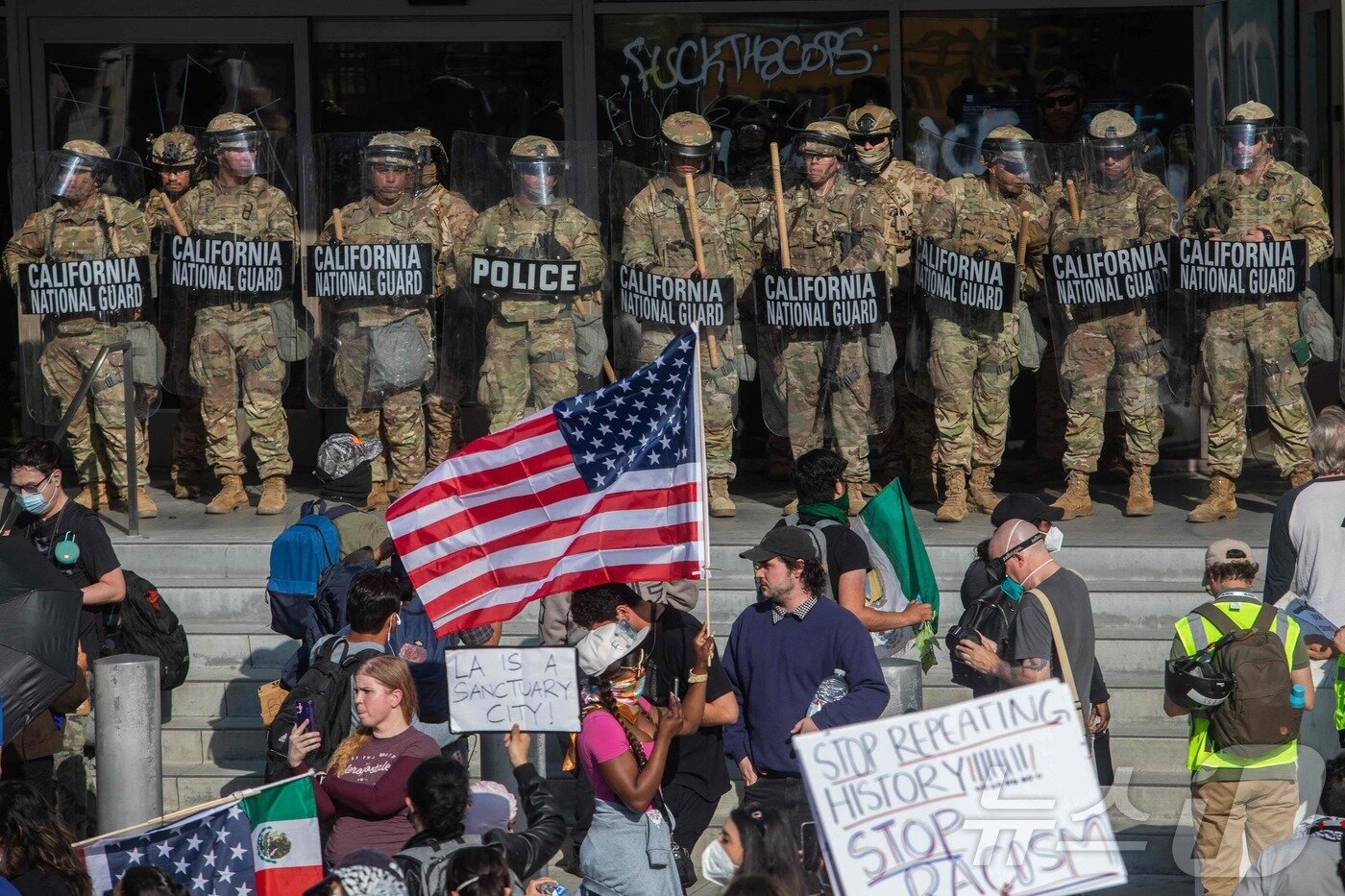 본문 이미지 - 2025년 6월 9일&#40;현지시간&#41; 로스앤젤레스에서 연방 이민 작전에 반대하는 시위대가 연방 건물 밖에서 경비를 서고 있는 캘리포니아 주방위군 대원들을 향해 피켓과 깃발을 들고 있다. ⓒ AFP=뉴스1 ⓒ News1 신기림 기자