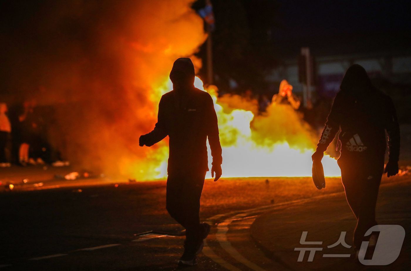본문 이미지 - 북아일랜드 밸리미나에서 벌어진 반(反) 이민 시위에서 복면을 쓴 시위대가 11일(현지시간) 방화 현장을 빠져나오고 있다. 2025.6.11 ⓒ AFP=뉴스1 ⓒ News1 김경민 기자