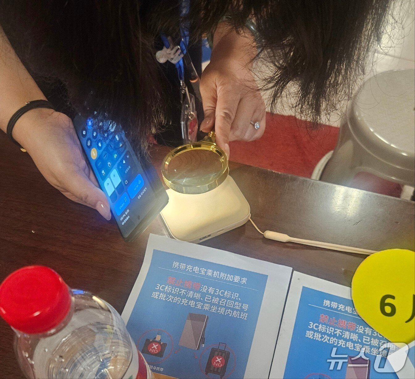 본문 이미지 - 29일 중국 지린성 옌지 공항 관계자가 보조배터리의 'CCC' 표기를 확인하기 위해 돋보기를 들고 있다.