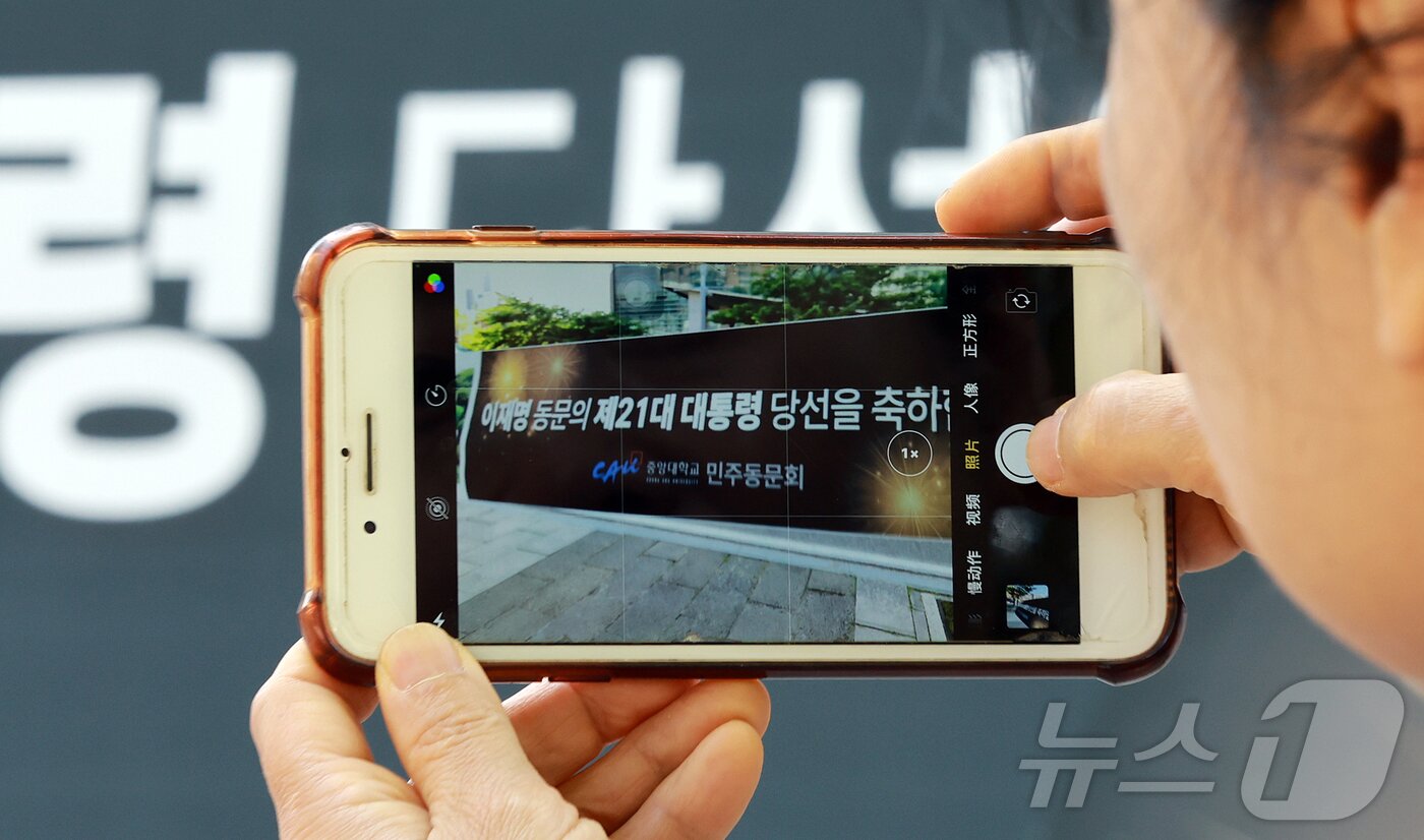 본문 이미지 - 4일 이재명 대통령의 모교인 서울 동작구 중앙대학교에서 한 시민이 당선 축하 현수막을 스마트폰으로 촬영하고 있다. 이 대통령은 1728만7513표를 얻어 득표율 49.42%로 당선됐다. 2025.6.4/뉴스1 ⓒ News1 김진환 기자