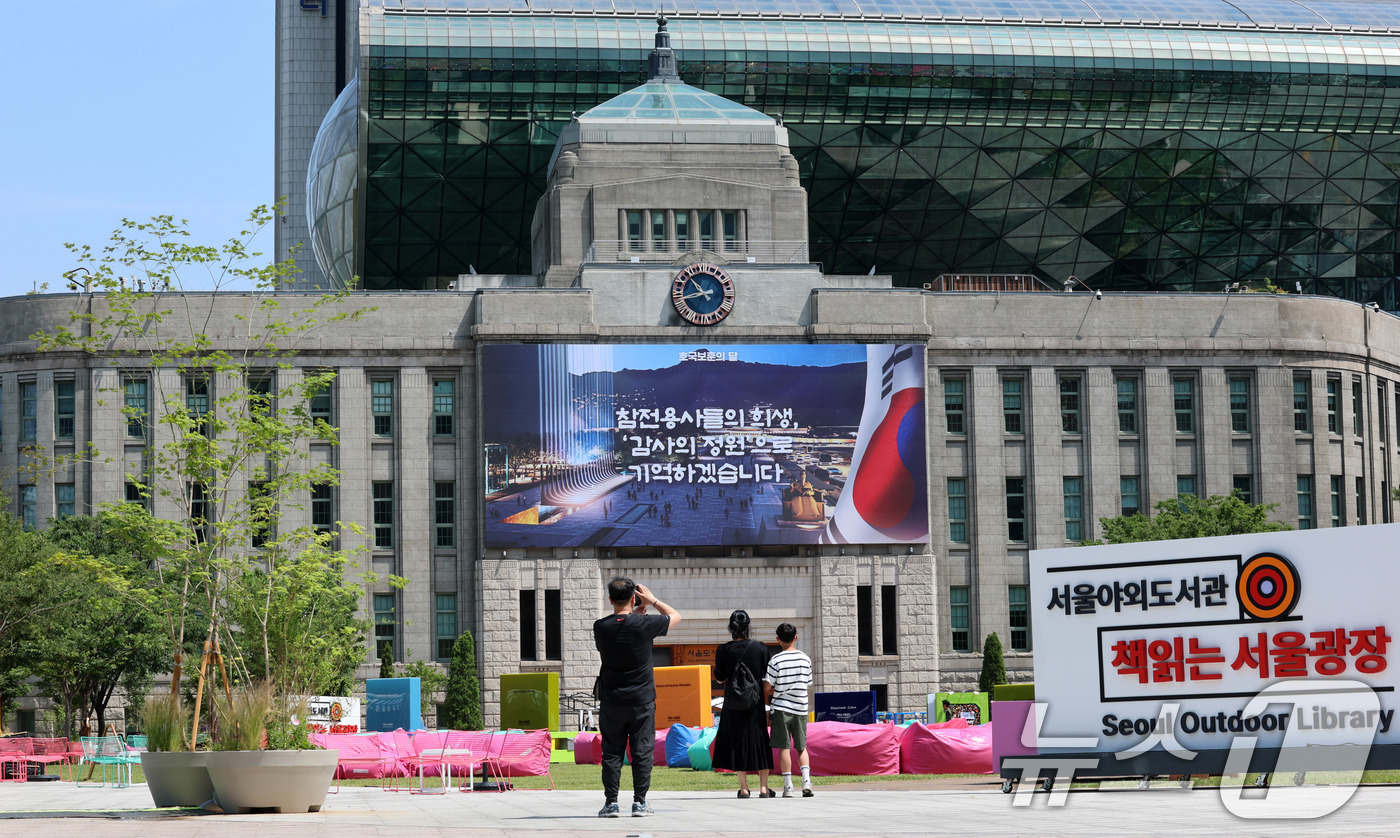 (서울=뉴스1) 박세연 기자 = 현충일인 6일 서울 중구 서울광장을 찾은 한 가족이 호국보훈의달을 맞이해 새로 단장된 서울도서관 외벽 대형 글판 서울꿈새김판을 배경으로 기념사진을 …