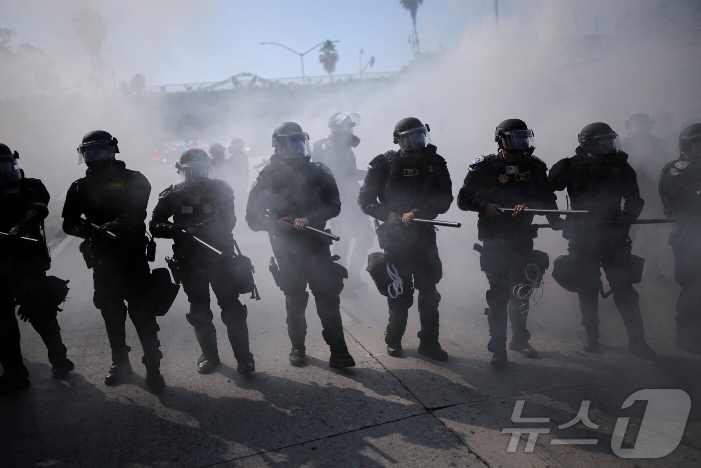 본문 이미지 - 8일(현지시간) 미국 LA에서 열린 연방 이민법 집행에 대한 항의 시위에서 경찰관들이 최루탄 속에서 진압봉을 들고 이동하고 있다.ⓒ 로이터=뉴스1