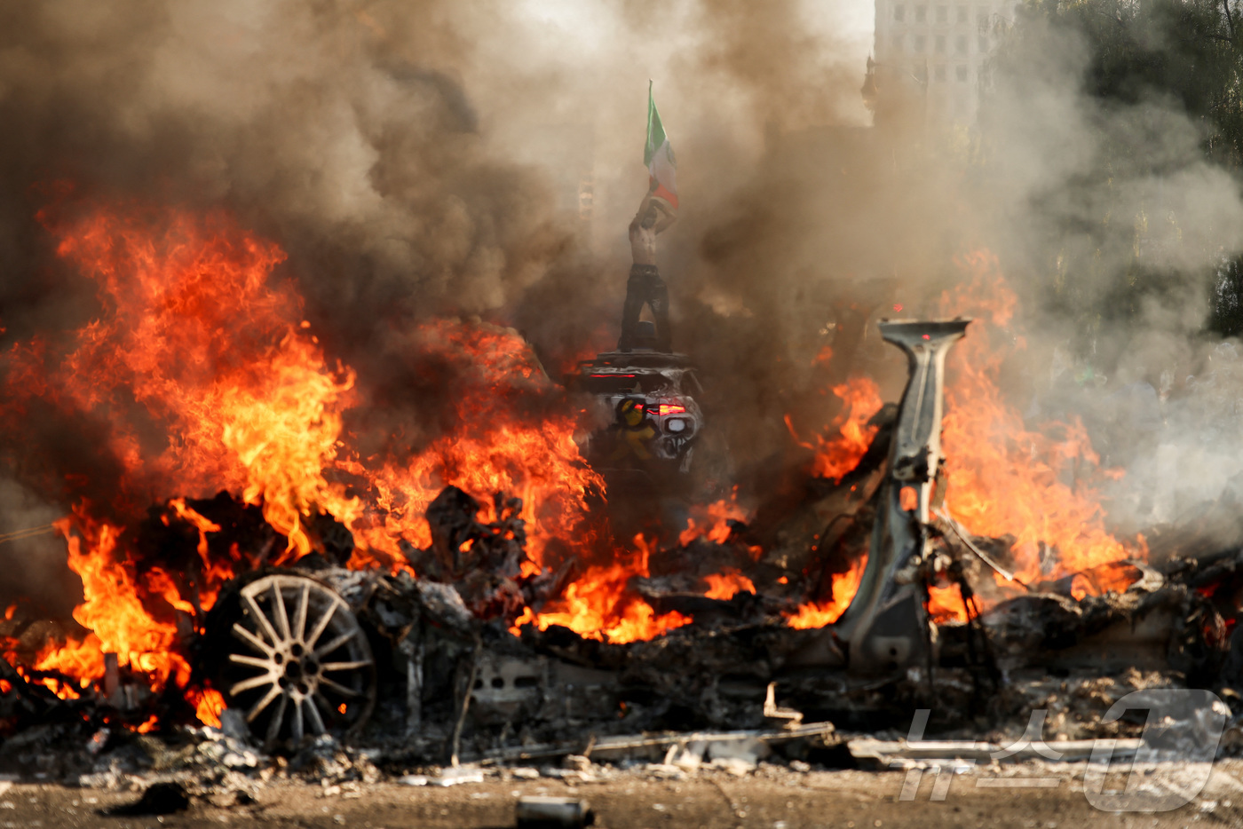 8일(현지시간) 미국 캘리포니아주 LA 시청 인근에서 열린 연방 이민 단속에 항의하는 시위에서 한 남자가 불타는 차량 뒤에서 멕시코 국기를 흔들고 있다.ⓒ 로이터=뉴스1