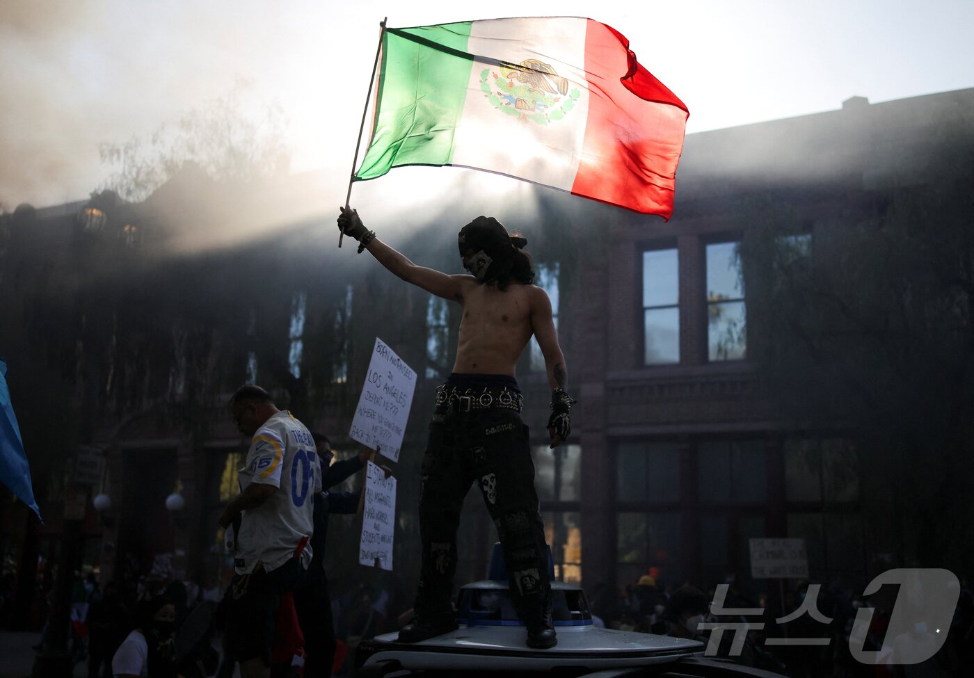 본문 이미지 - 8일(현지시간) 미국 캘리포니아주 LA 시청 인근에서 열린 연방 이민 단속에 항의하는 시위에서 한 남자가 멕시코 국기를 흔들고 있다.ⓒ 로이터=뉴스1