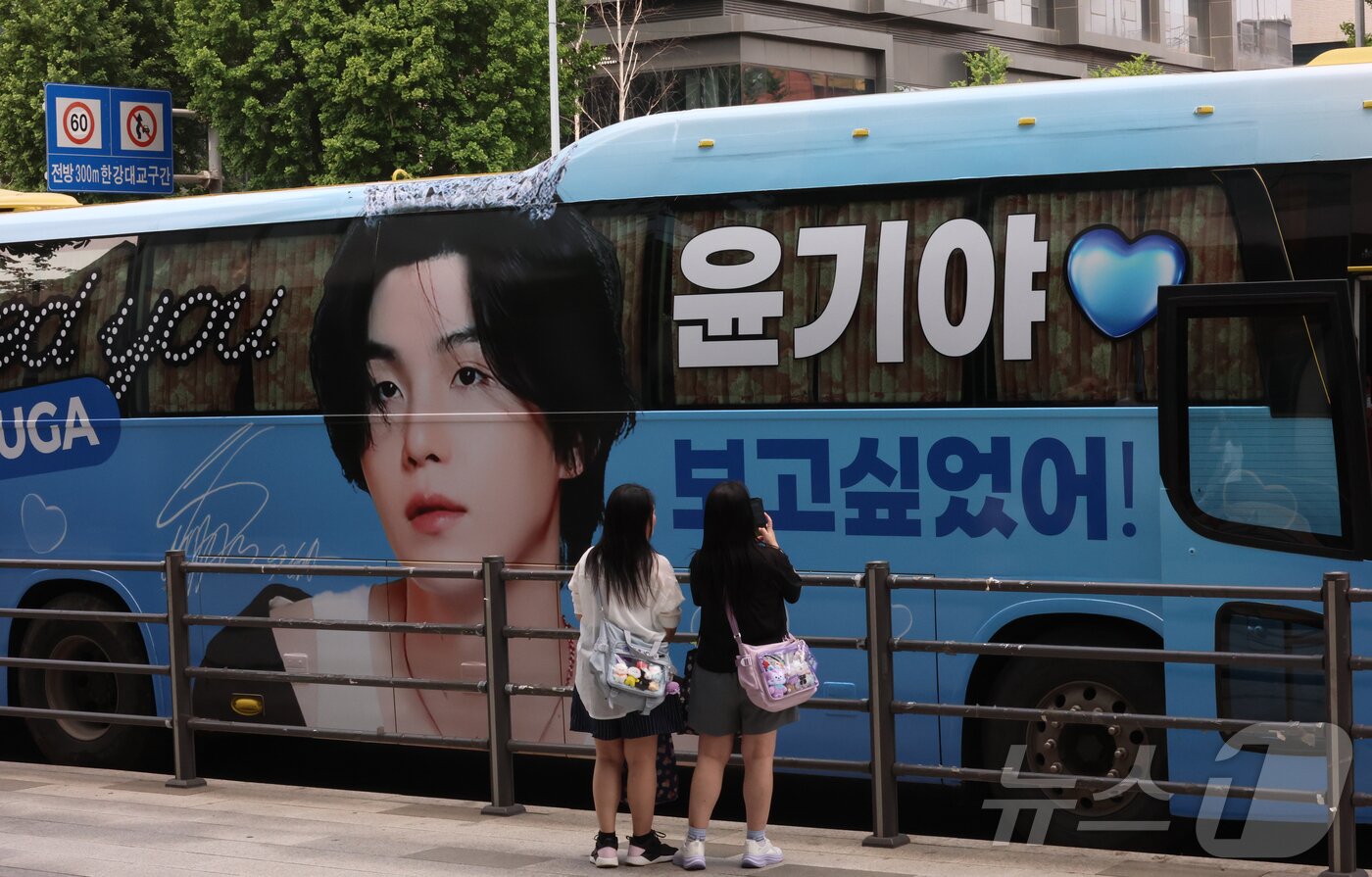 본문 이미지 - 9일 오전 서울 용산구 하이브 사옥 앞에서 방탄소년단&#40;BTS&#41; 글로벌 팬들&#40;아미&#41;이 멤버들의 제대를 기대하며 기념 촬영을 하고 있다. 2023년 12월 입대한 그룹 방탄소년단&#40;BTS&#41;의 RM, 뷔, 지민, 정국이 이번 주 육군 현역 복무를 마치고 만기 전역한다. 2025.6.9/뉴스1 ⓒ News1 권현진 기자