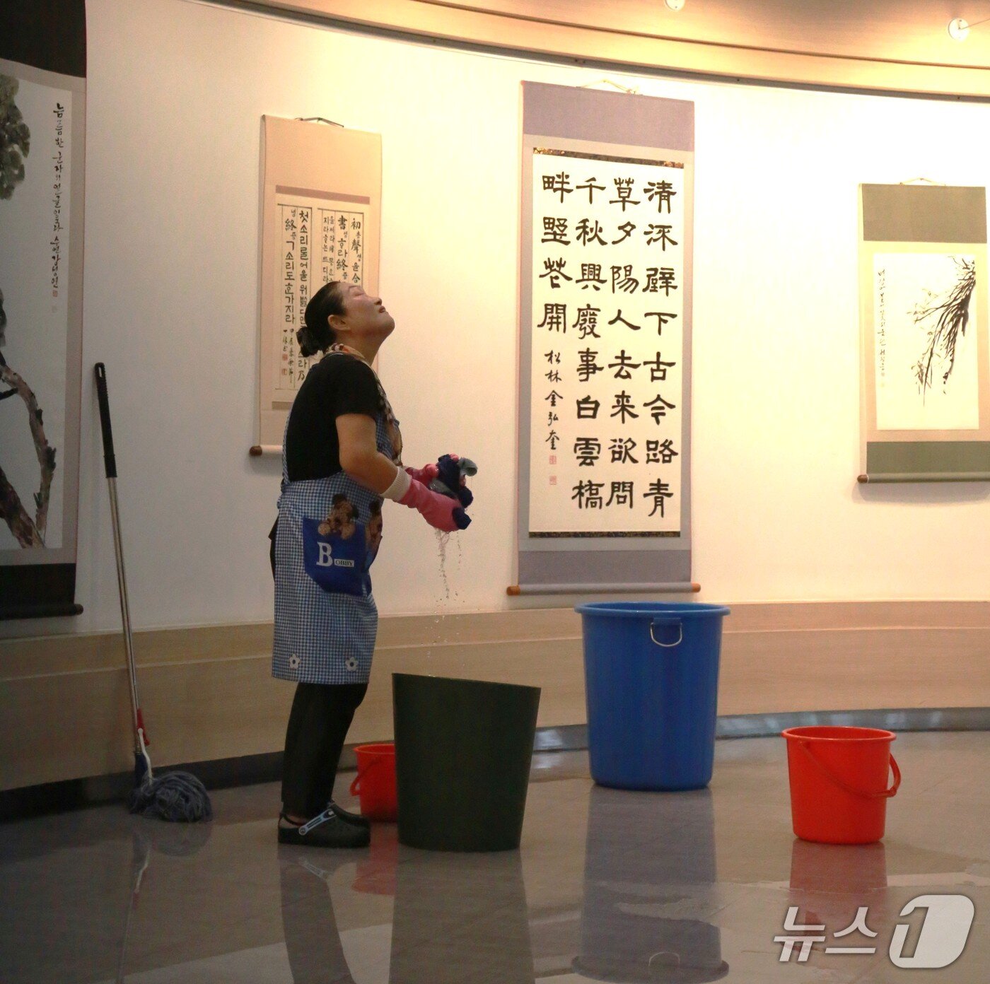 본문 이미지 - 17일 제천시민회관 직원이 1층 전시관에서 양동이로 빗물을 받고 있다. 직원이 천장에서 떨어지고 있는 빗물을 바라보고 있다.2025.7.17./뉴스1 ⓒ News1 손도언 기자  