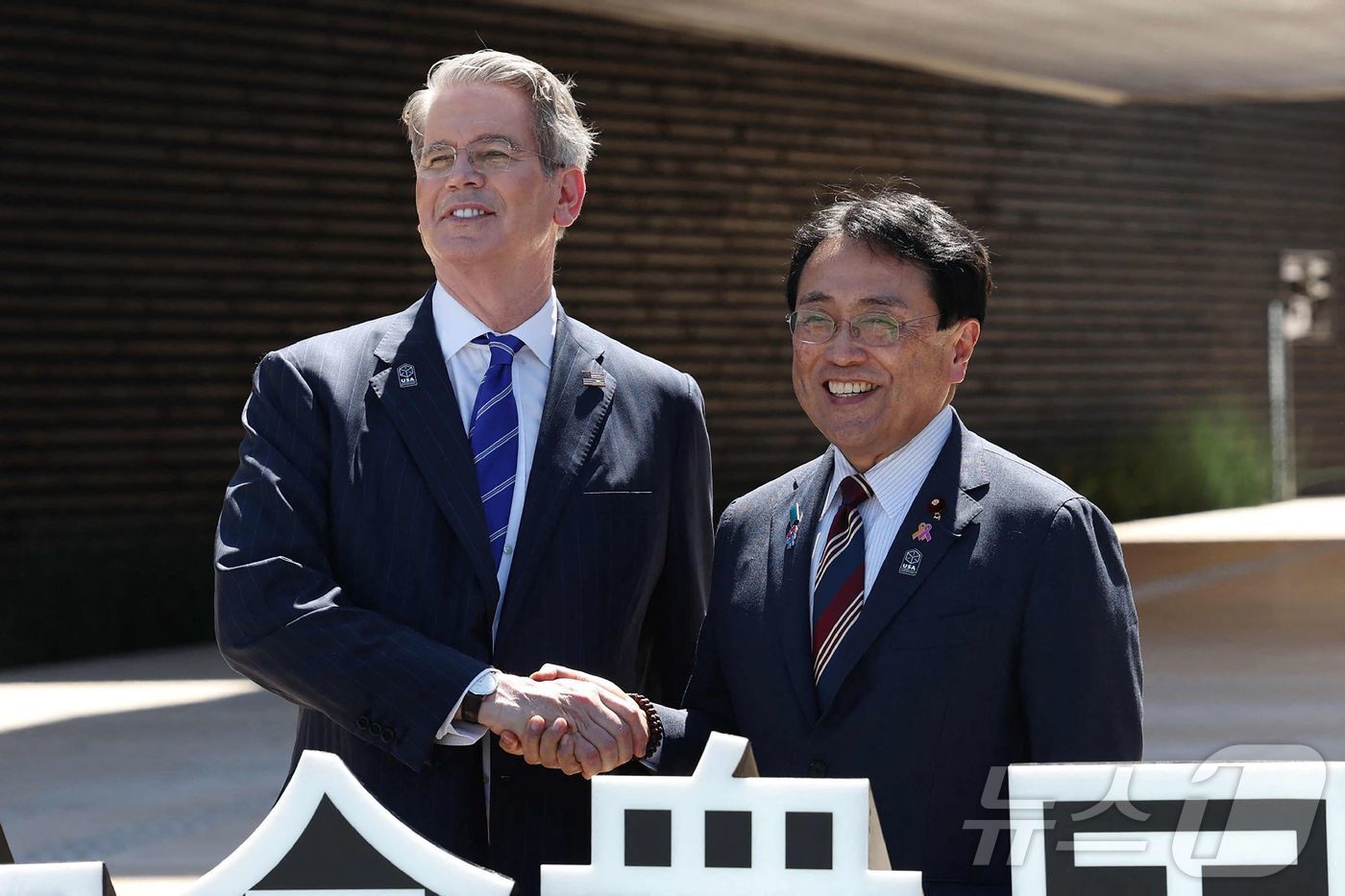 본문 이미지 - 스콧 베선트 미국 재무장관(왼쪽)이 19일 오사카 엑스포 미국관 앞에서 열린 미국 국가의 날 행사에 참석하며, 일본의 경제 재생 담당 장관이자 관세 협상의 수석 협상가인 아카자와 료세이(오른쪽)와 악수하고 있다. 2025.07.19.ⓒ AFP=뉴스1