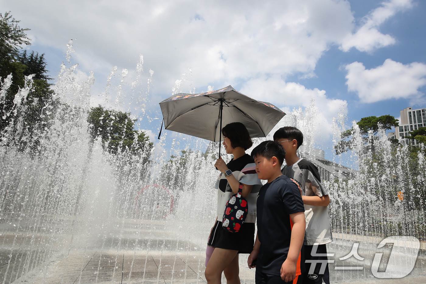 (대구=뉴스1) 공정식 기자 = 오전부터 폭염이 시작된 23일 대구 서구 서부도서관 앞 평리공원에서 양산을 쓴 가족이 바닥분수 물줄기 옆을 지나고 있다. 2025.7.23/뉴스1