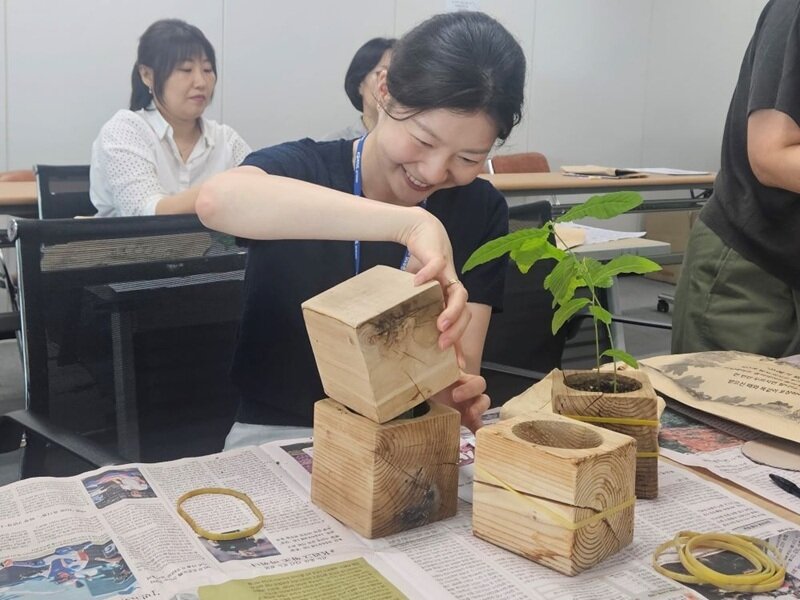 본문 이미지 - 코레일네트웍스 임직원들이 도토리 묘목을 노을공원에 기증하기 위해 봉사활동 개시 때 받았던 화분 뚜껑, 포장지, 고무줄을 재활용하여 포장하고 있다. / 사진=코레일네트웍스 제공