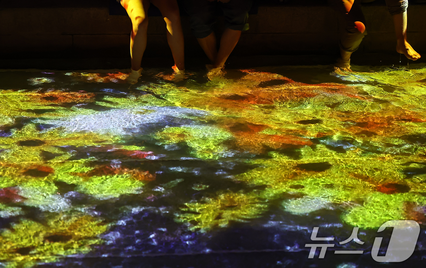 (서울=뉴스1) 김도우 기자 = 무더위가 이어진 23일 서울 중구 청계천을 찾은 시민들이 수면 미디어아트를 보며 더위를 식히고 있다. 2025.7.23/뉴스1