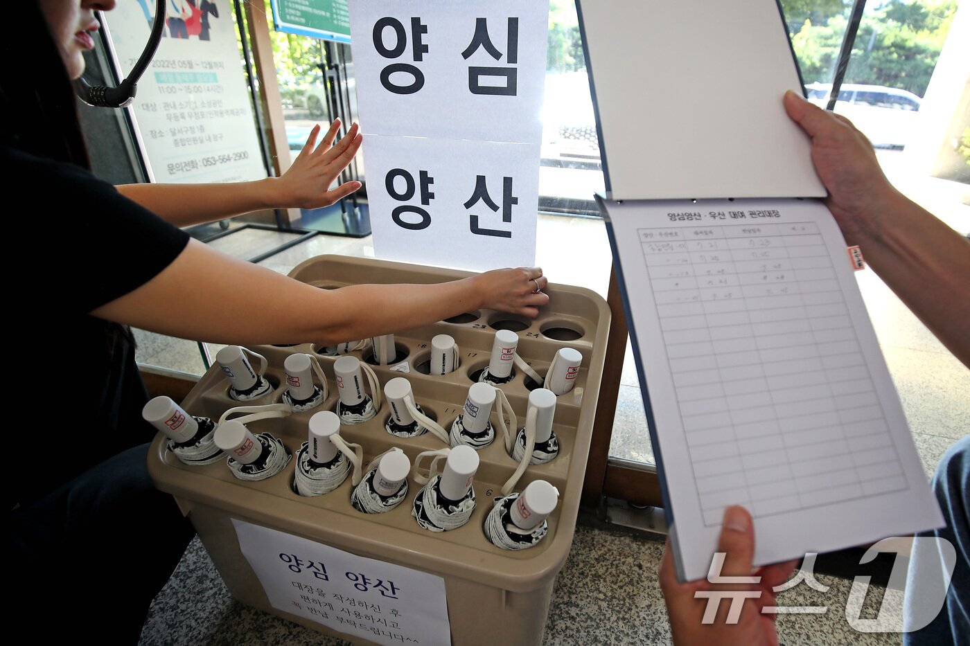 본문 이미지 - 폭염이 이어진 28일 오전 대구 달서구청 직원들이 민원실에서 양산꽂이 앞에 &#39;양심양산&#39; 안내문을 붙이고 있다. &#39;양심에 맡기자&#39;는 취지로 빌려주는 이 양산은 이용자가 관리대장을 작성하지 않는 경우가 많아 회수율이 낮다. 2025.7.28/뉴스1 ⓒ News1 공정식 기자