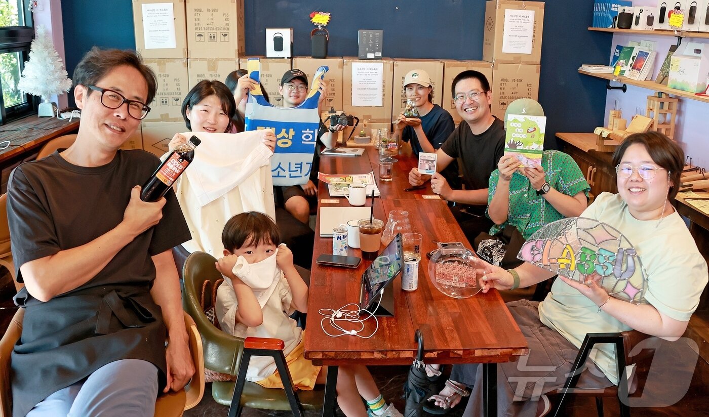 본문 이미지 - 충북 괴산군 칠성면 옛 칠성시장 골목 '칠리단길'에 입점한 청년 창업자들이 각 상점의 상징물을 들고 카페 로컬즈에서 포즈를 취했다.(괴산군 제공).2025.7.29. 2025.7.29/뉴스1