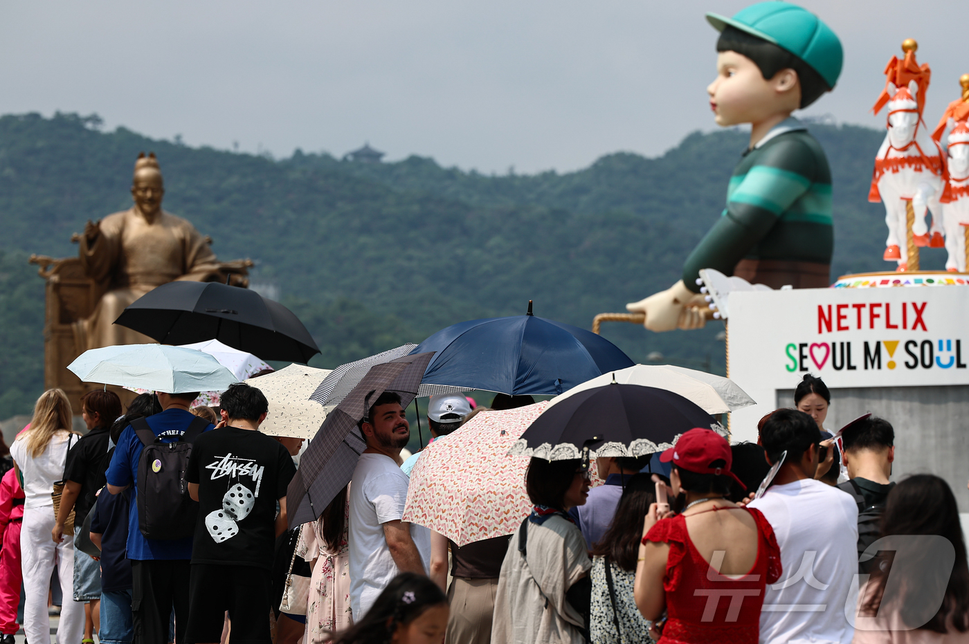 (서울=뉴스1) 김도우 기자 = 무더위가 이어진 4일 서울 종로구 광화문광장에 마련된 넷플릭스 오징어 게임 체험존에 관광객들이 양산을 쓰고 대기하고 있다. 2025.7.4/뉴스1