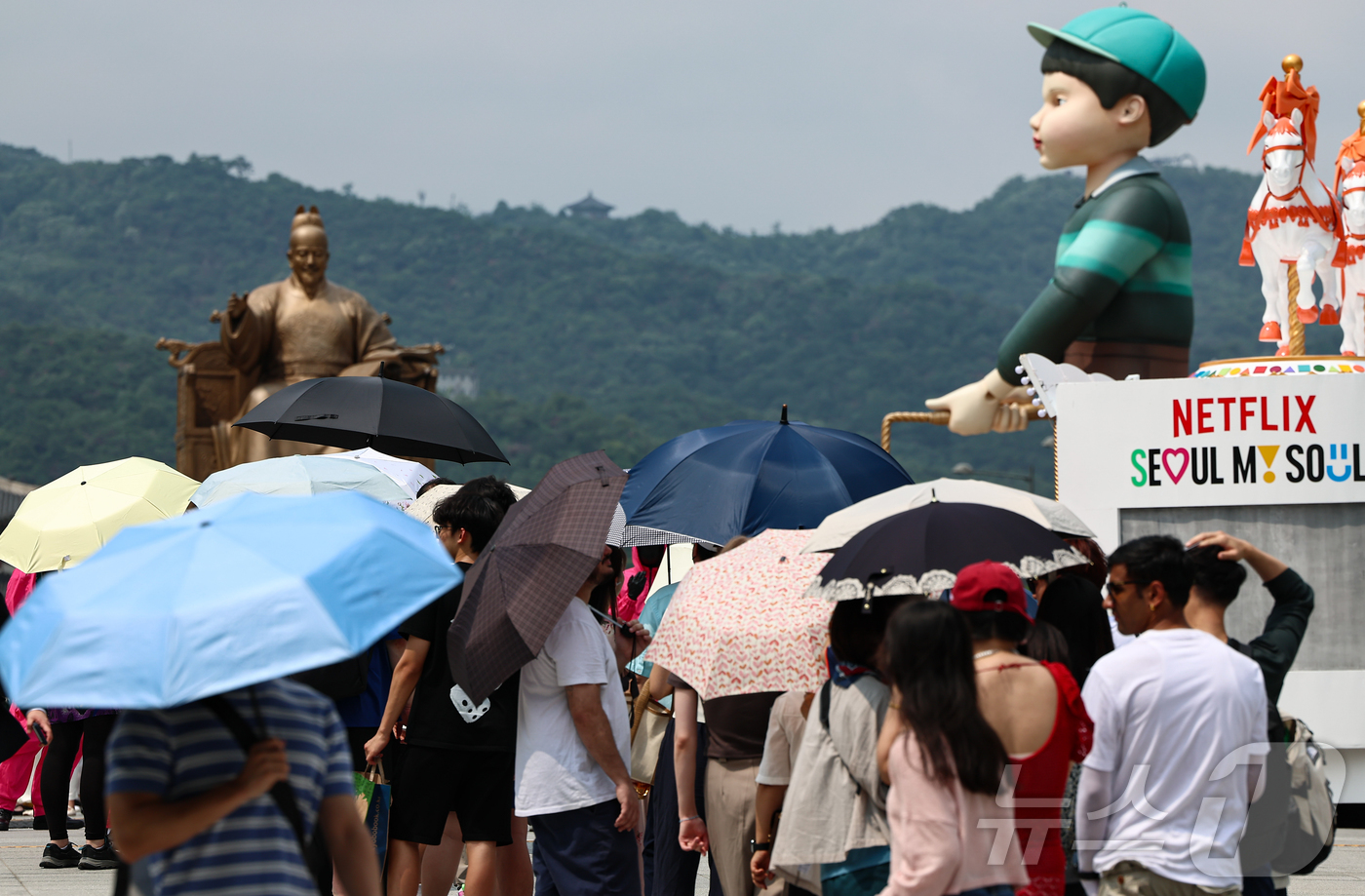(서울=뉴스1) 김도우 기자 = 무더위가 이어진 4일 서울 종로구 광화문광장에 마련된 넷플릭스 오징어 게임 체험존에 관광객들이 양산을 쓰고 대기하고 있다. 2025.7.4/뉴스1