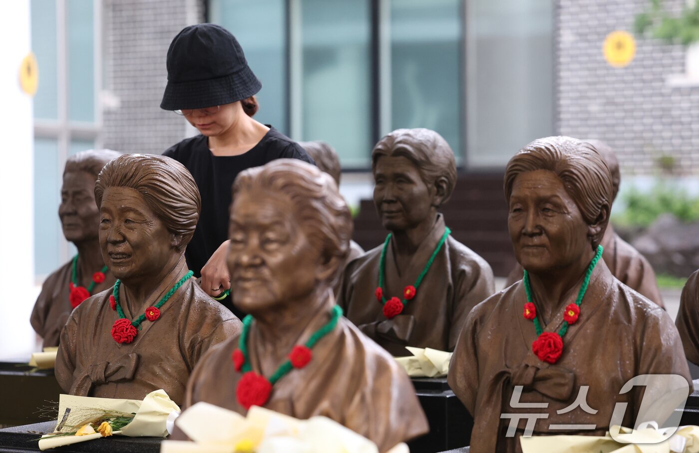 본문 이미지 - &#39;일본군 위안부 피해자 기림의 날&#39;인 14일 경기 광주시 퇴촌면 나눔의집에서 한 시민이 위안부 피해자 할머니들의 흉상에 직접 뜨개질한 동백꽃 목걸이를 걸고 있다. ⓒ News1 김영운 기자