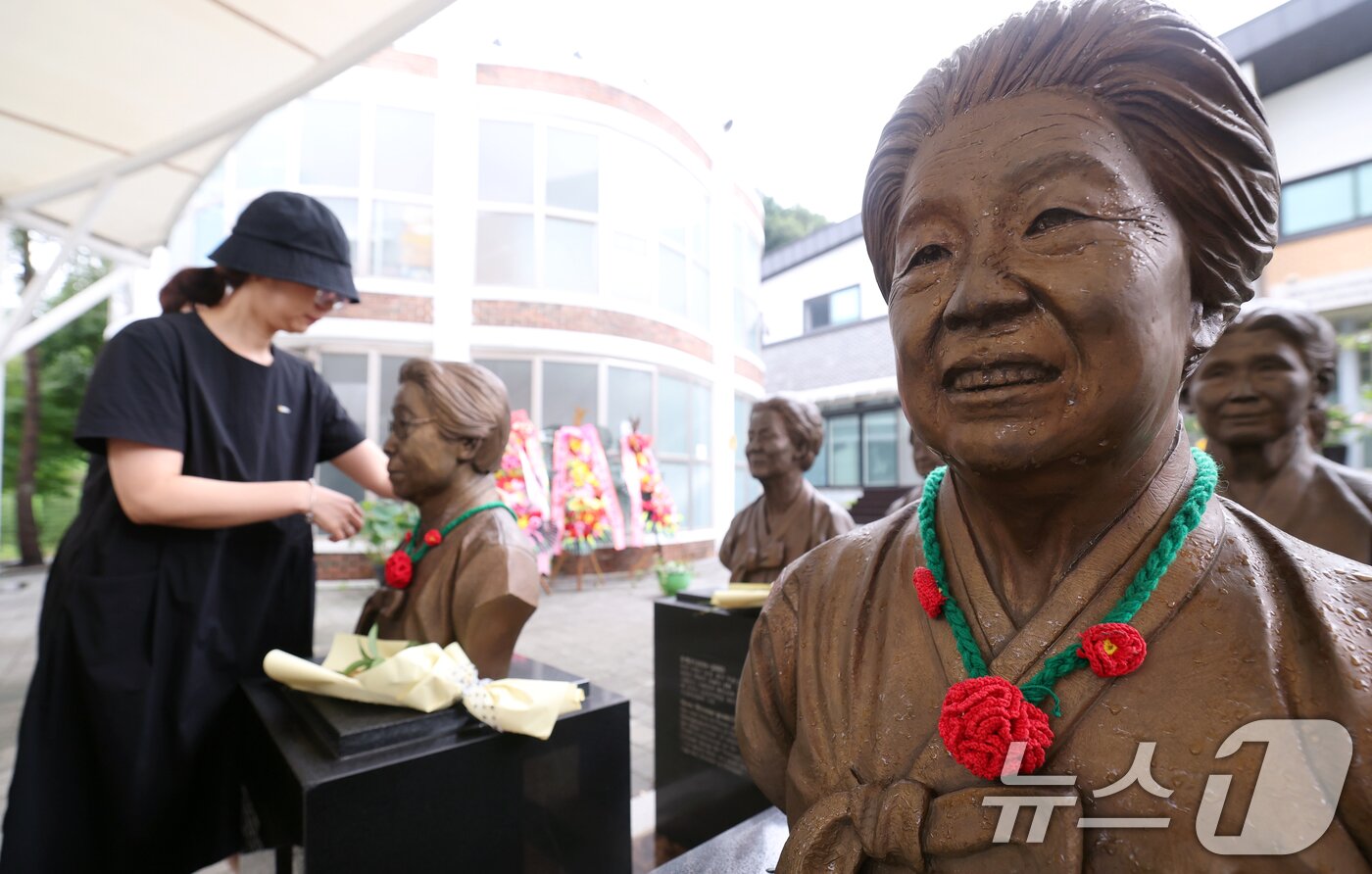 본문 이미지 - &#39;일본군 위안부 피해자 기림의 날&#39;인 14일 경기 광주시 퇴촌면 나눔의집에서 한 시민이 위안부 피해자 할머니들의 흉상에 직접 뜨개질한 동백꽃 목걸이를 걸고 있다.  ⓒ News1 김영운 기자
