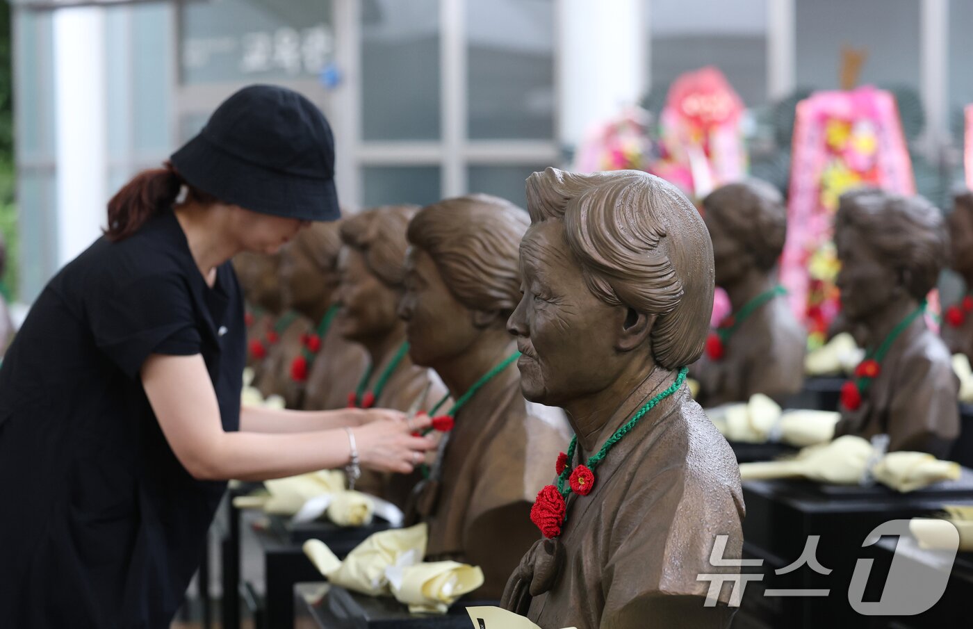 본문 이미지 - &#39;일본군 위안부 피해자 기림의 날&#39;인 14일 경기 광주시 퇴촌면 나눔의집에서 한 시민이 위안부 피해자 할머니들의 흉상에 직접 뜨개질한 동백꽃 목걸이를 걸고 있다.  ⓒ News1 김영운 기자