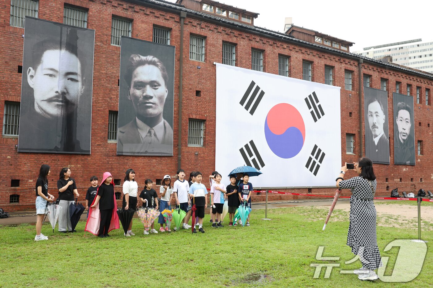 본문 이미지 - 제80주년 광복절을 하루 앞둔 14일 서울 서대문형무소역사관을 찾은 어린이들이 독립운동가들의 모습을 담은 현수막과 태극기를 배경으로 기념촬영을 하고 있다. 2025.8.14/뉴스1 ⓒ News1 민경석 기자