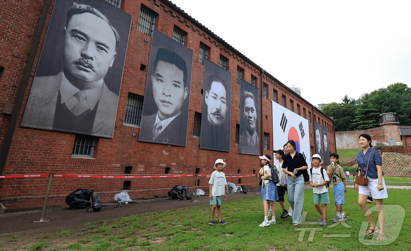 본문 이미지 - 제80주년 광복절인 15일 서울 서대문형무소역사관을 찾은 어린이들과 관람객들이 대형 태극기와 독립운동가들의 얼굴이 담긴 현수막 앞을 지나고 있다. 2025.8.15/뉴스1 ⓒ News1 김진환 기자