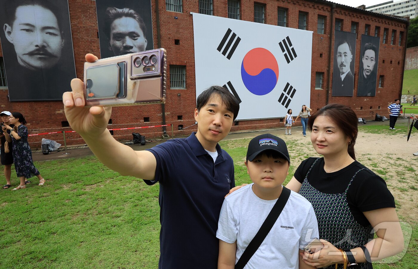 본문 이미지 - 제80주년 광복절인 15일 서울 서대문형무소역사관을 찾은 어린이들과 관람객들이 대형 태극기와 독립운동가들의 얼굴이 담긴 현수막 앞에서 기념 셀카를 찍고 있다. 2025.8.15/뉴스1 ⓒ News1 김진환 기자