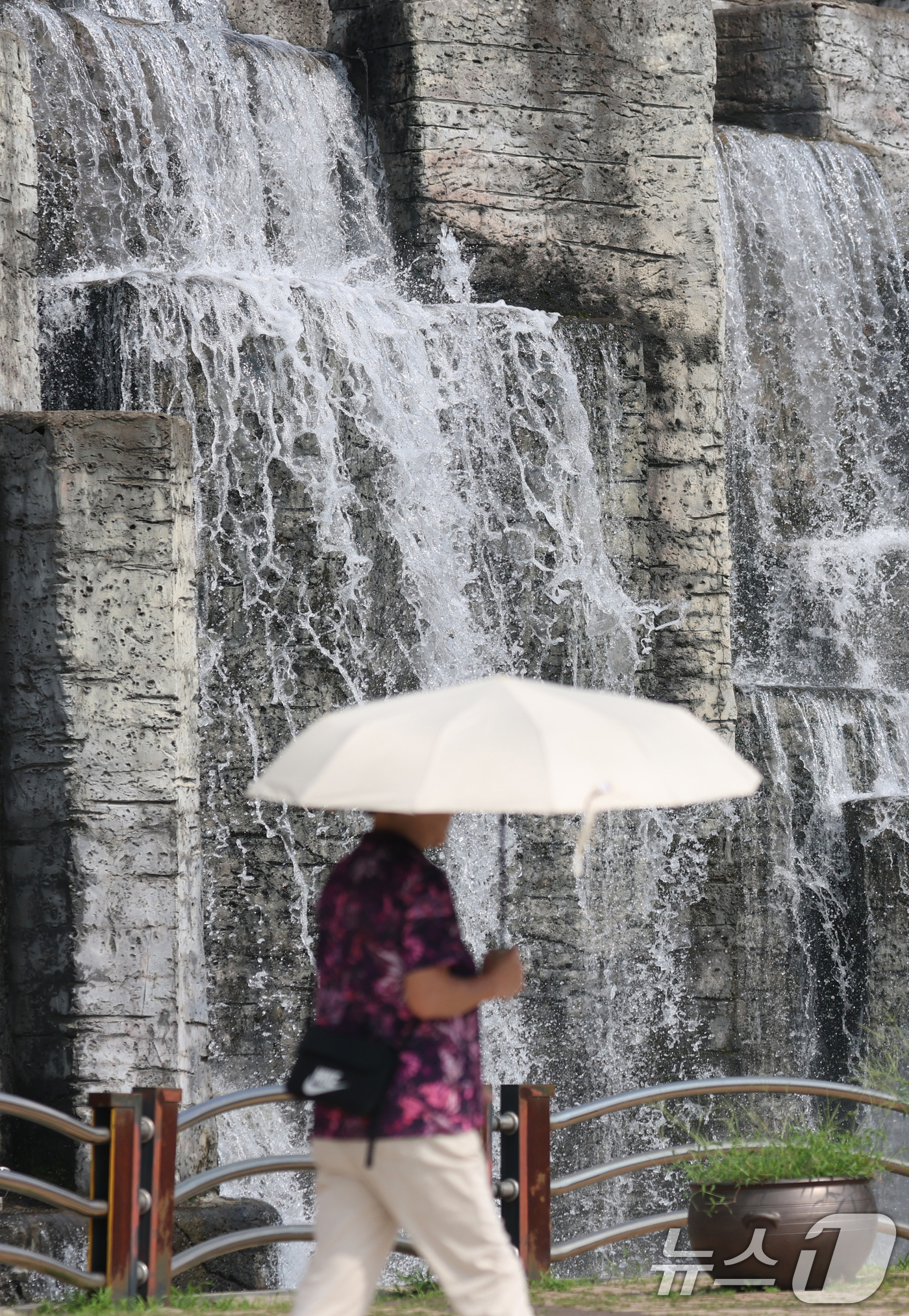 (오산=뉴스1) 김영운 기자 = 전국 대부분 지역에 폭염 경보나 주의보가 이어지고 있는 가운데 18일 오후 경기 오산시 수청공원에서 시민들이 시원하게 쏟아지는 폭포 앞으로 지나가고 …