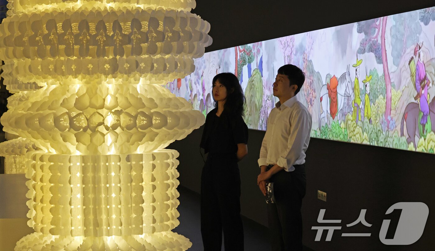 본문 이미지 - 19일 서울 동대문구 동대문디자인플라자(DDP)에서 열린 국가유산 활용 디지털 콘텐츠 전시 '헤리티지: 더 퓨처 판타지' 언론 공개회에서 방문객들이 1795년 정조의 수원행차를 담은 '화성행행도' 미디어아트에 영감을 받아 제작한 텍스타일 아티스트 이선의 설치 작품을 관람하고 있다.  2025.8.19/뉴스1 ⓒ News1 오대일 기자