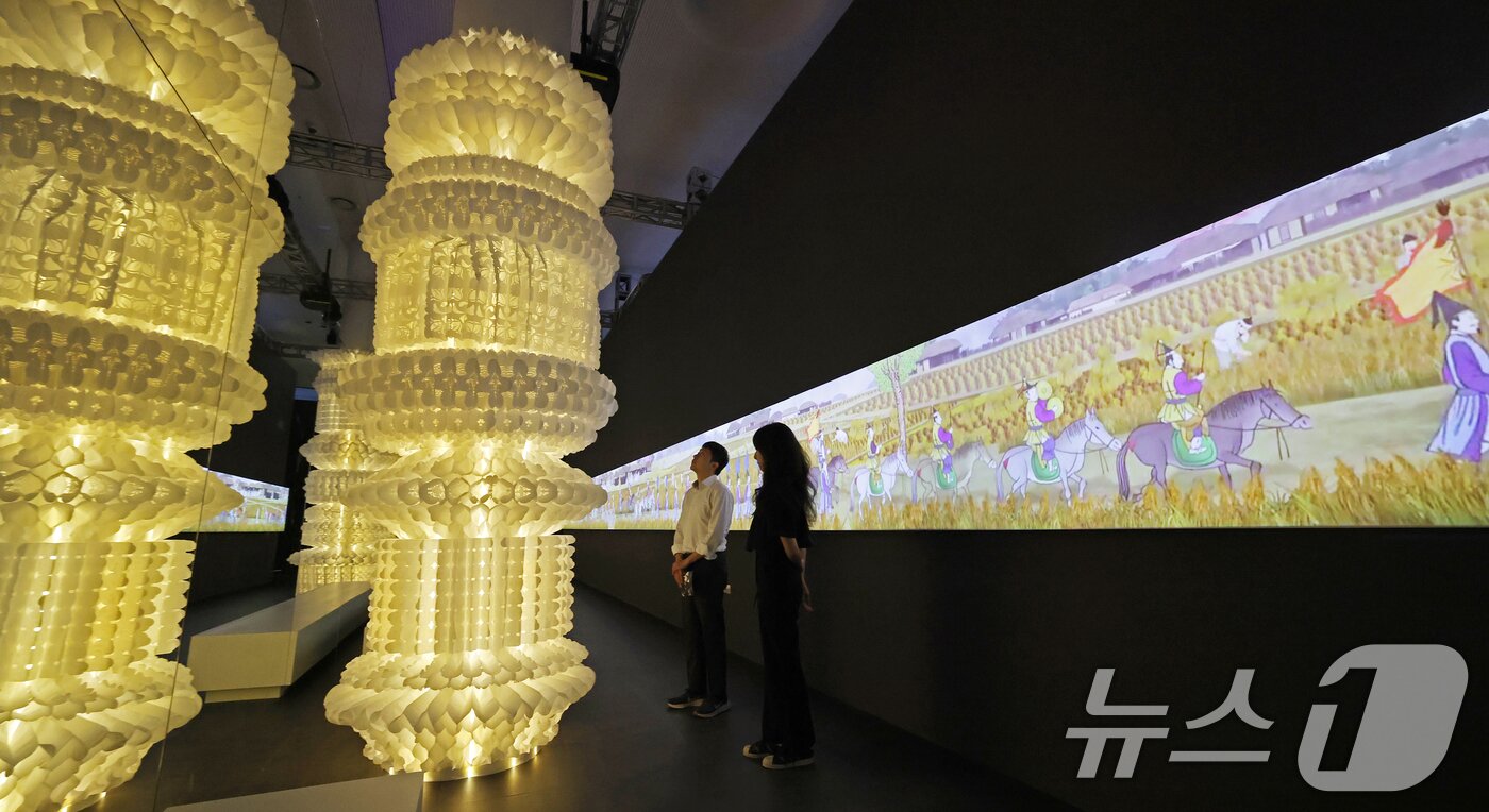 본문 이미지 - 19일 서울 동대문구 동대문디자인플라자(DDP)에서 열린 국가유산 활용 디지털 콘텐츠 전시 '헤리티지: 더 퓨처 판타지' 언론 공개회에서 방문객들이 1795년 정조의 수원행차를 담은 '화성행행도' 미디어아트에 영감을 받아 제작한 텍스타일 아티스트 이선의 설치 작품을 관람하고 있다.  2025.8.19/뉴스1 ⓒ News1 오대일 기자