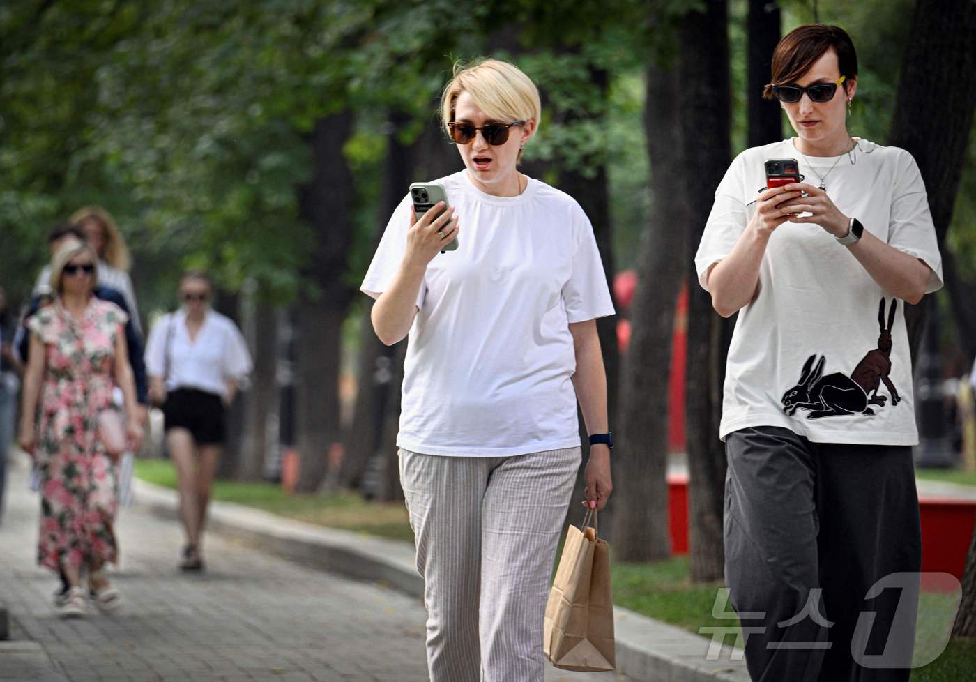 (모스크바 AFP=뉴스1) 권영미 기자 = 2025년 7월 30일 러시아 모스크바에서 선글라스를 착용한 보행자들이 스마트폰을 사용하는 모습. 러시아는 최근 언론의 자유와 온라인 표 …