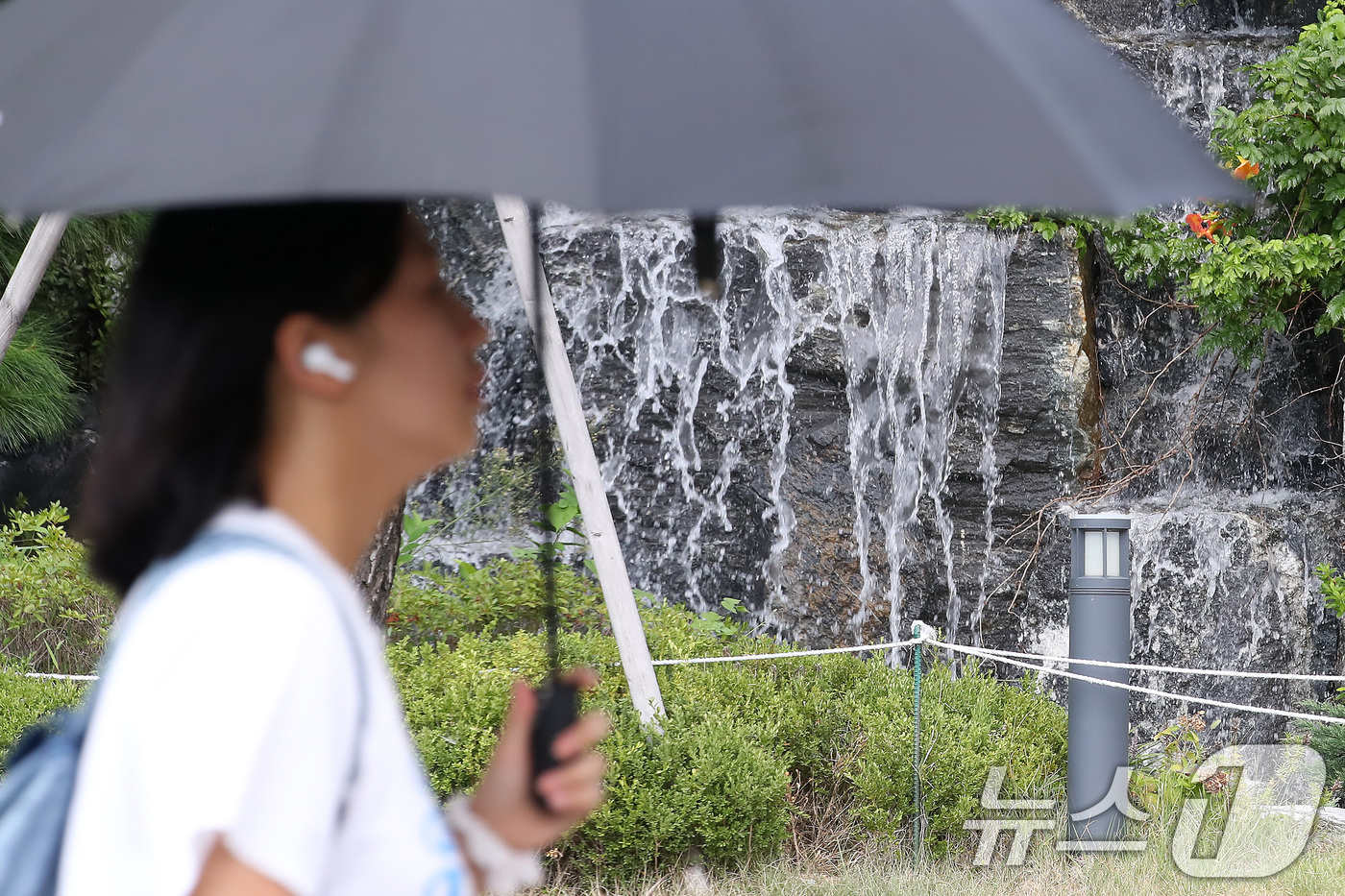 (대구=뉴스1) 공정식 기자 = 폭염이 계속된 28일 오후 대구 북구의 한 아파트 단지에서 양산을 쓴 시민이 인공폭포 앞을 지나고 있다. 2025.8.28/뉴스1