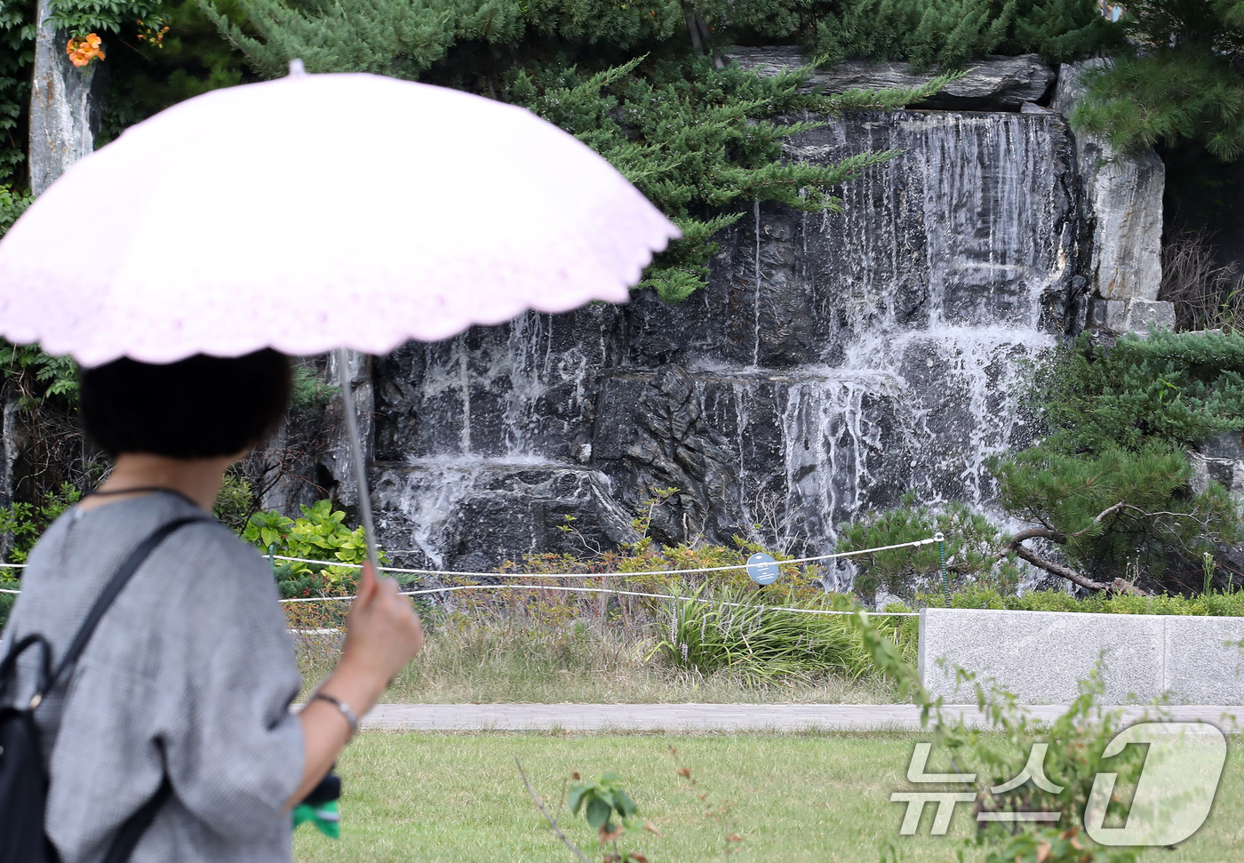 (대구=뉴스1) 공정식 기자 = 폭염이 계속된 28일 오후 대구 북구의 한 아파트 단지에서 양산을 쓴 시민이 인공폭포 앞을 지나고 있다. 2025.8.28/뉴스1
