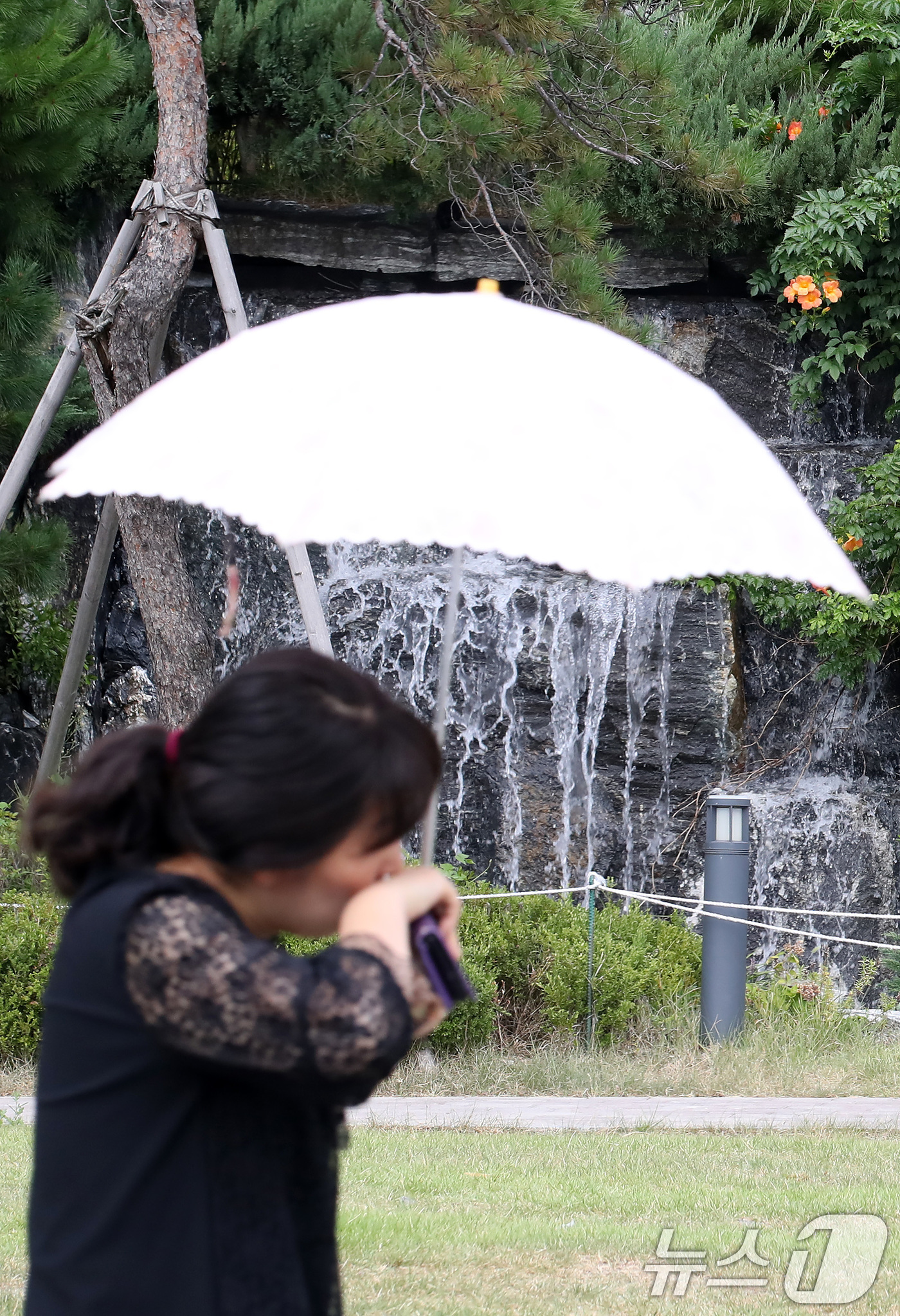 (대구=뉴스1) 공정식 기자 = 폭염이 계속된 28일 오후 대구 북구의 한 아파트 단지에서 양산을 쓴 시민이 인공폭포 앞을 지나고 있다. 2025.8.28/뉴스1