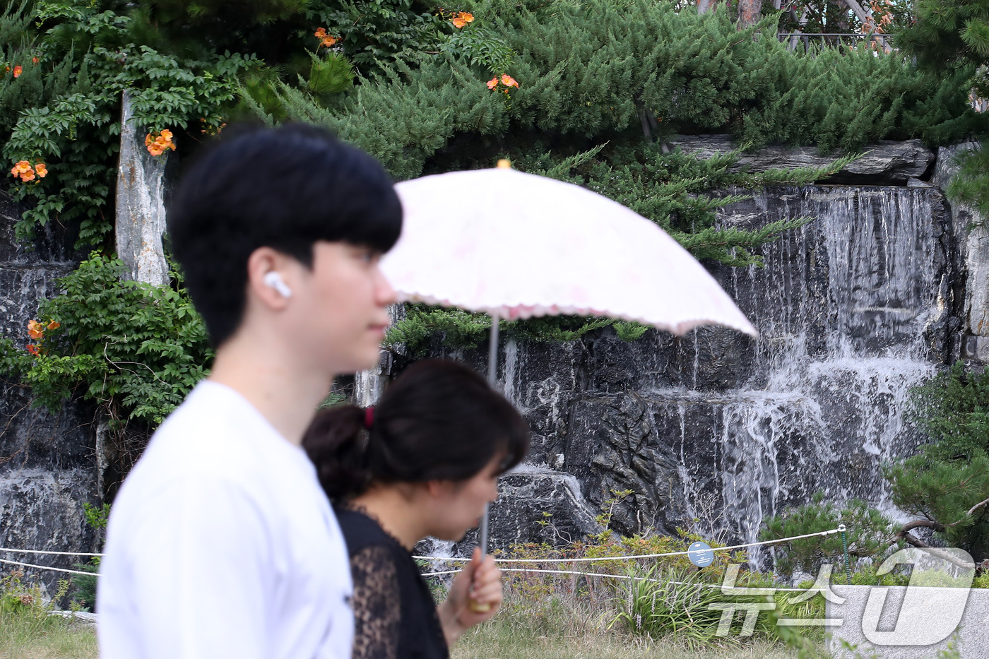 (대구=뉴스1) 공정식 기자 = 폭염이 계속된 28일 오후 대구 북구의 한 아파트 단지에서 양산을 쓴 시민이 인공폭포 앞을 지나고 있다. 2025.8.28/뉴스1