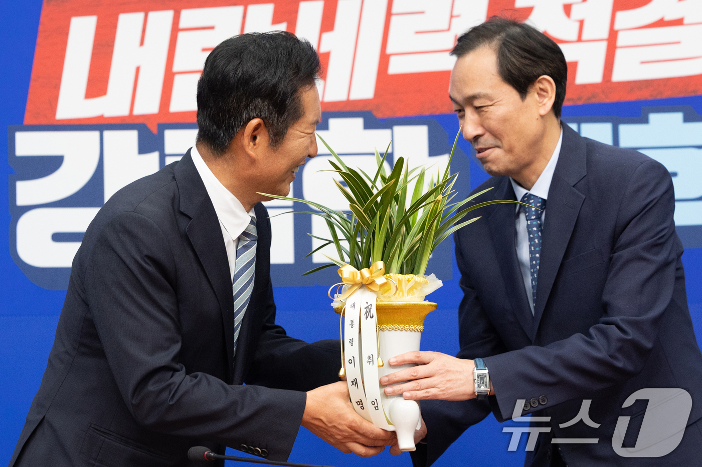 (서울=뉴스1) 이승배 기자 = 정청래 더불어민주당 신임 대표가 4일 오후 서울 여의도 국회에서 우상호 대통령실 정무수석으로부터 대통령 축하 난을 받고 있다. 2025.8.4/뉴스 …