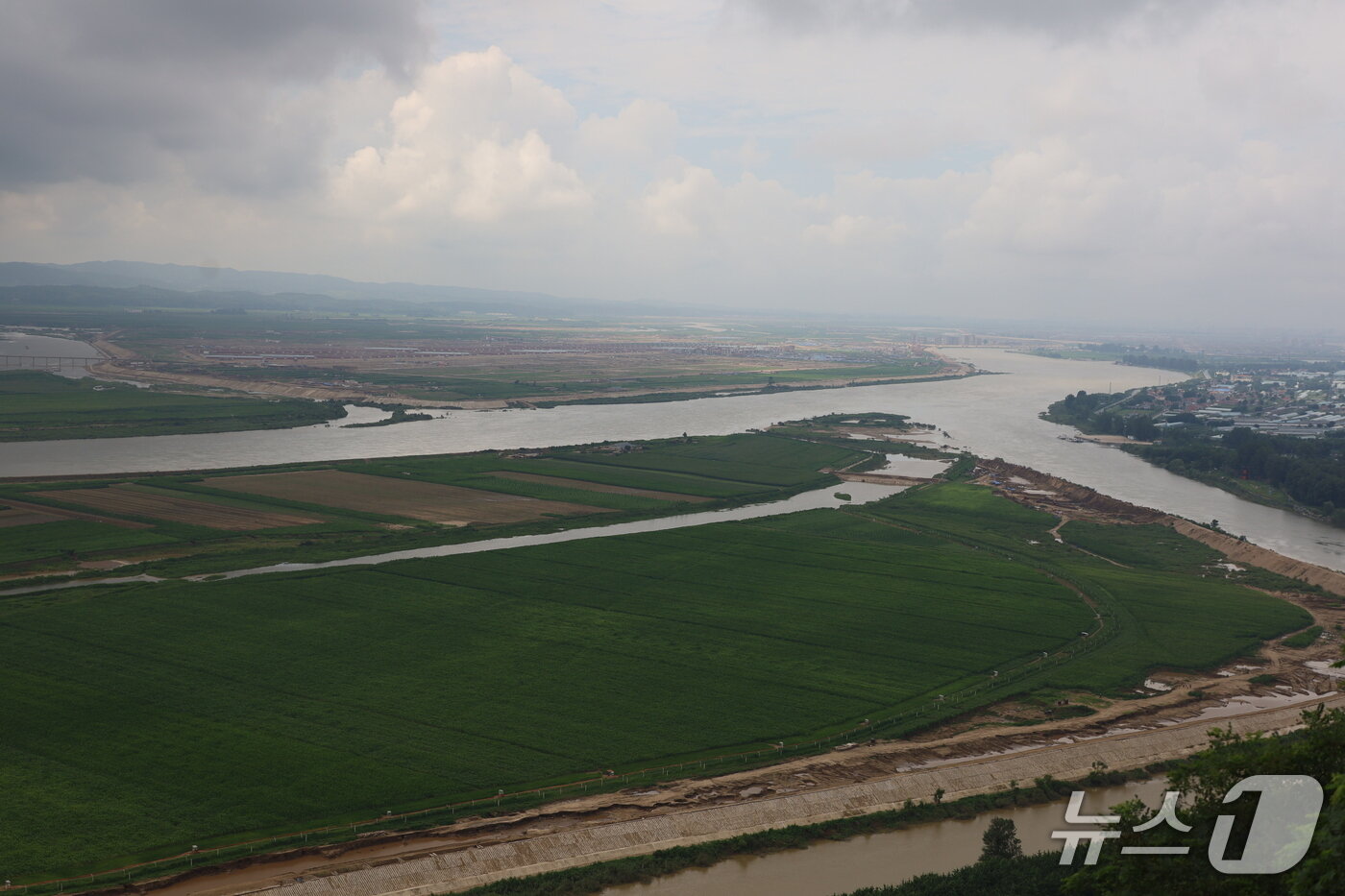 본문 이미지 - 중국 랴오닝성 단둥시 후산에서 본 의주군 어적도와 서호리, 신의주시 위화도의 모습. 앞쪽의 섬이 제방공사가 한창인 어적도이고, 강 건너편 중앙에 온실농장이 건설 중인 서호리가 자리하고 있다. 압록강 하류 쪽으로 멀리 새 주택단지가 조성된 위화도가 보인다. &#40;평화경제연구소 제공&#41; 