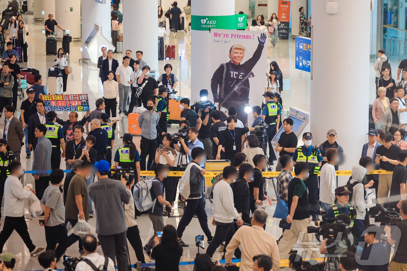 본문 이미지 - 12일 인천국제공항 입국장에서 미국 이민당국에 의해 체포·구금됐다 풀려나 입국한 우리 국민들 너머로 이제석 이제석광고연구소 대표가 트럼프 미국 대통령의 모습이 담긴 플랜카드 퍼포먼스를 벌이고 있다. (공동취재)2025.9.12/뉴스1 ⓒ News1 박지혜 기자