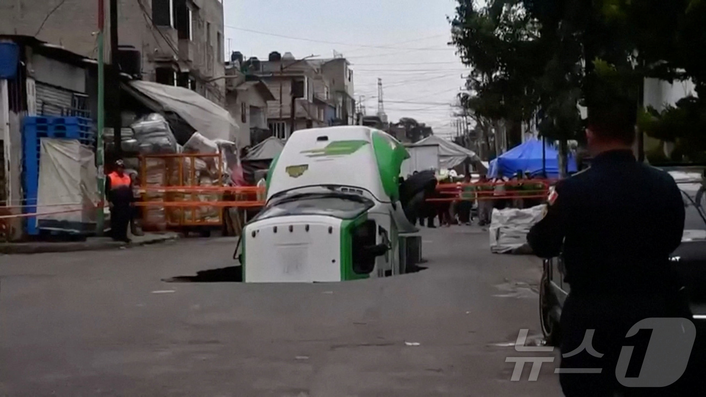 (멕시코시티 로이터=뉴스1) 권영미 기자 = 13일(현지시간) 멕시코 멕시코시티 이스타팔라파 지역에서 탄산음료 배달 트럭이 싱크홀에 빠졌다. 한 시민이 이를 지켜보고 있다.ⓒ 로이 …