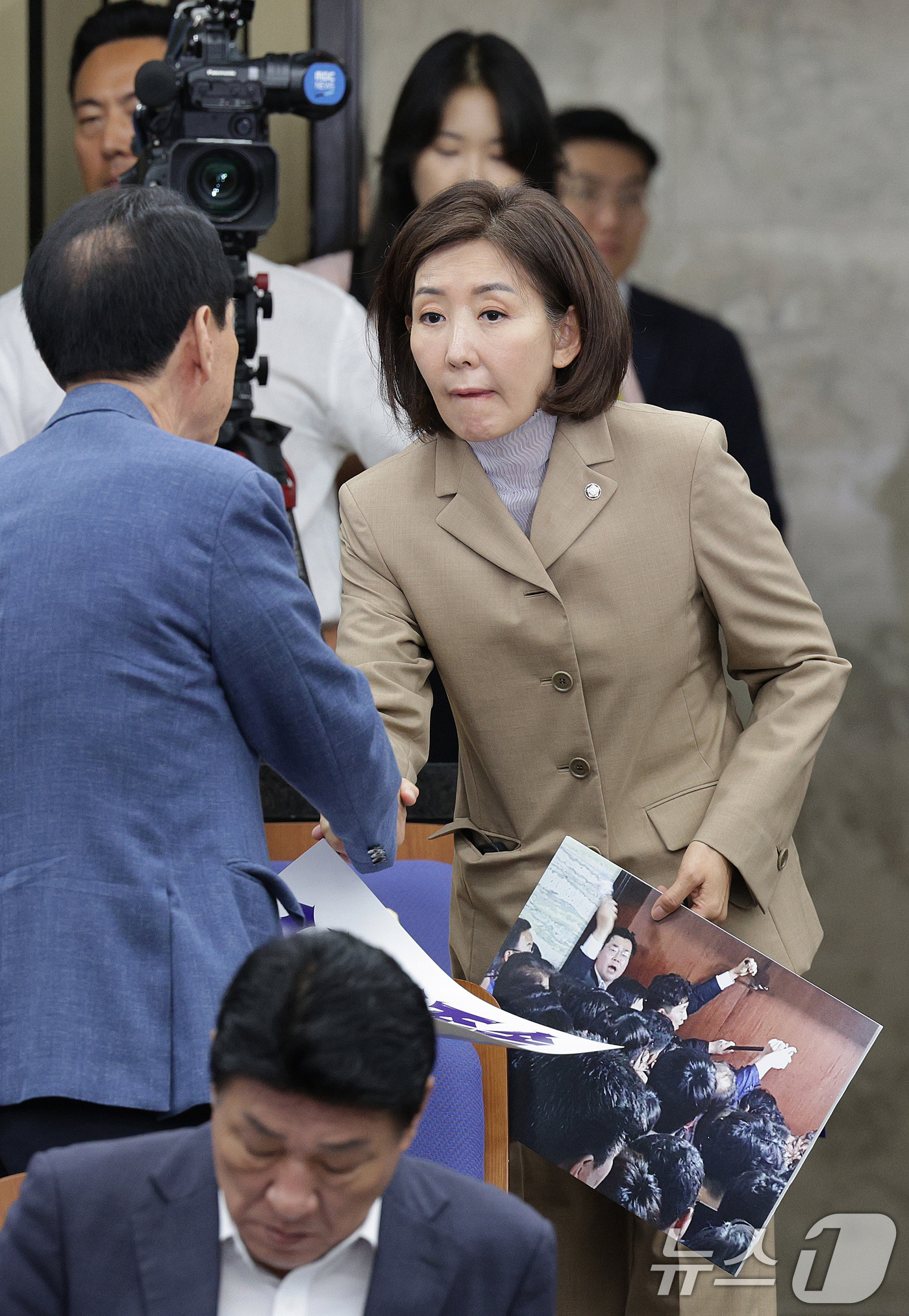 (서울=뉴스1) 신웅수 기자 = 나경원 국민의힘 의원이 16일 오전 서울 여의도 국회에서 열린 긴급 의원총회에서 빠루 사진을 들고 의원들과 인사하고 있다. 2025.9.16/뉴스1 …