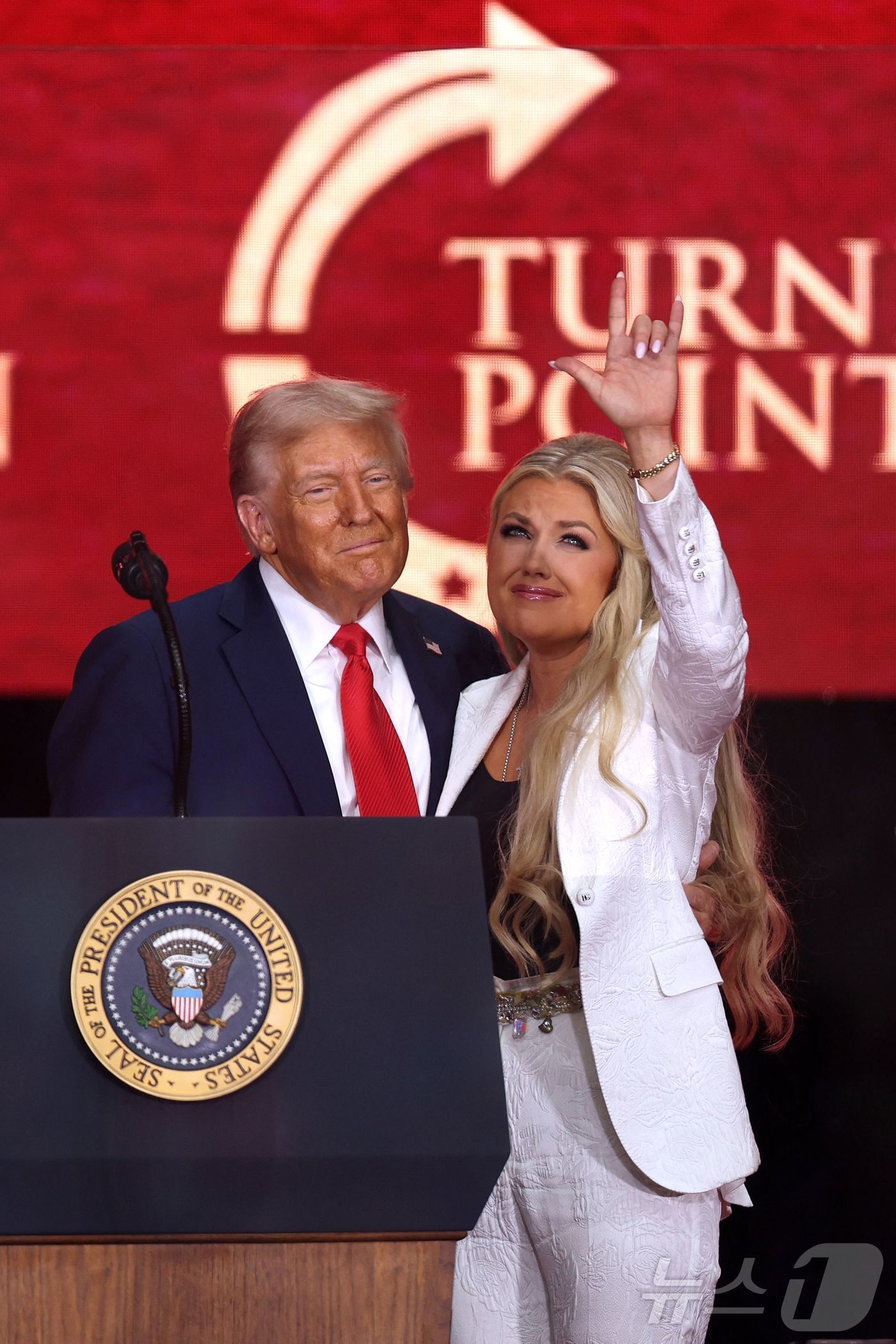 본문 이미지 - 총격으로 숨진 우파 활동가 찰리 커크의 아내 에리카 커크가 21일 애리조나주 글렌데일에서 열린 추모 행사에서 도널드 트럼프 대통령과 끌어안은 뒤 하늘을 향해 손동작을 하고 있다. 2025.9.21 ⓒ AFP=뉴스1 ⓒ News1 강민경 기자