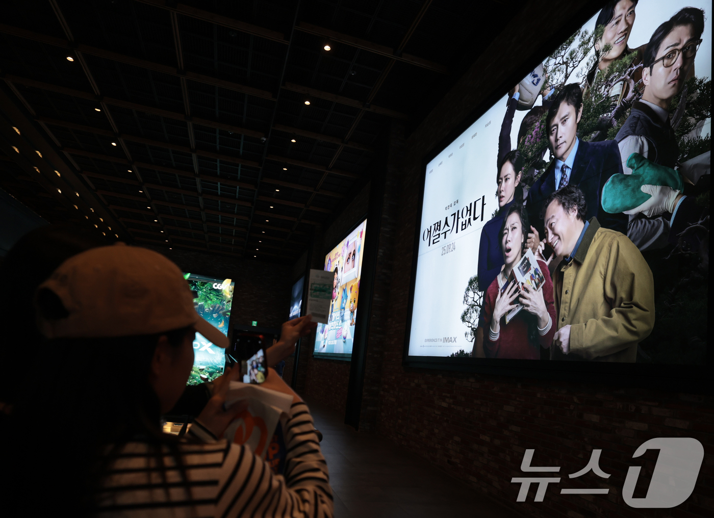 (서울=뉴스1) 권현진 기자 = 25일 서울도심의 한 영화관에서 관객이 박찬욱 감독의 영화 '어쩔수가없다' 포스터 사진을 찍고 있다.이날 영화진흥위원회 영화관 입장권 통합전산망 집 …