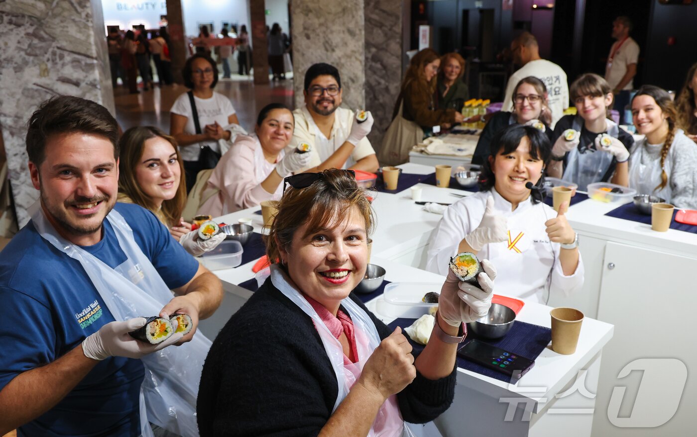 본문 이미지 - 29일&#40;현지시간&#41; 스페인 마드리드 아르테스 예술센터에서 열린 ‘2025 스페인 K-박람회’에서 한국농수산식품유통공사 ‘K-FOOD’ 부스 한식 쿠킹클래스 김밥 아틀리에에 참가한 현지인들이 김예림 셰프와 함께 만든 김밥을 들어 보이고 있다. &#40;사진가 우채연 제공, 재판매 및 DB금지&#41; 2025.9.30/뉴스1 ⓒ News1 이준성 기자