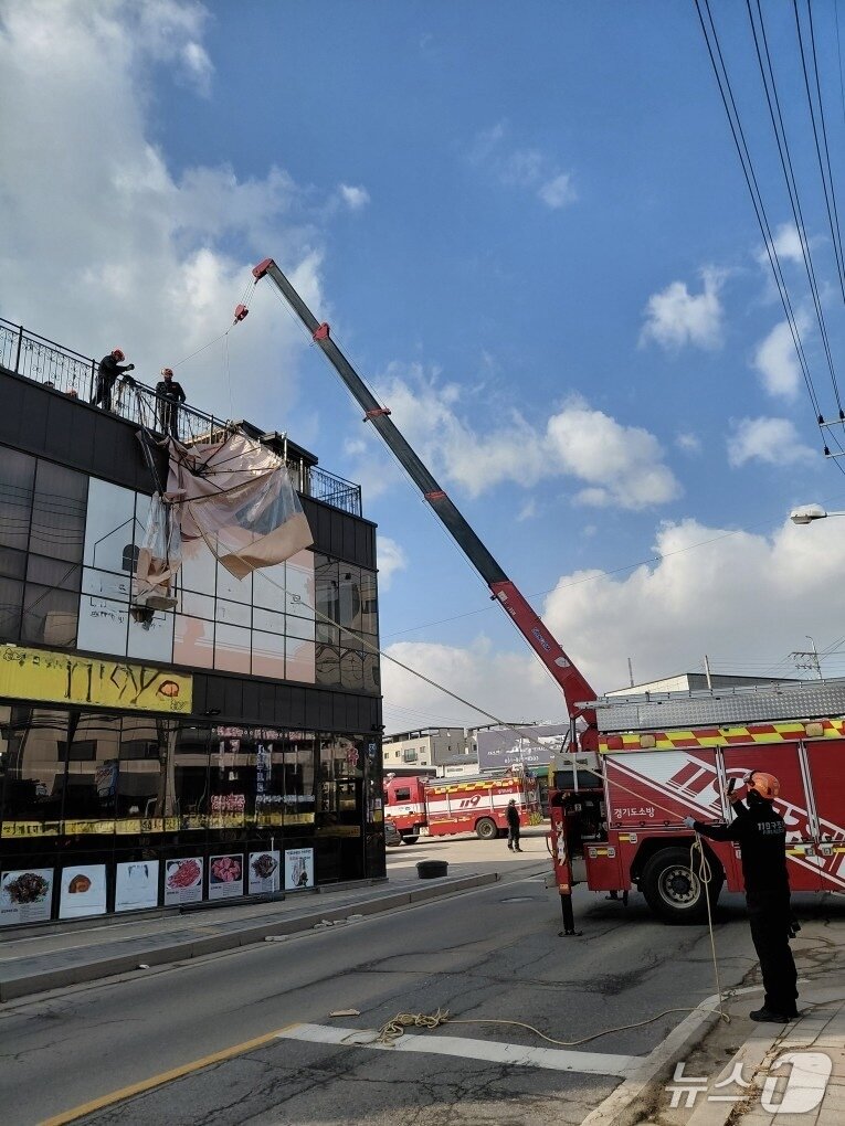 본문 이미지 - 경기 고양시 일산 옥상에 설치되어 있는 캐노피 천막 구조물이 강풍으로 탈락돼 소방당국이 크레인을 활용해 지상으로 인양 작업을 벌이고 있다. (경기소방재난본부 제공. 재판매 및 DB금지)